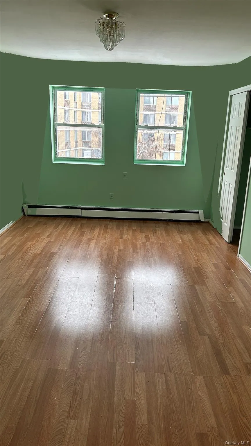 Empty room with healthy amount of natural light, wood finished floors, and baseboard heating Empty room with healthy amount of natural light, wood finished floors, and baseboard heating