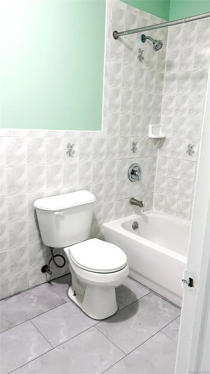 Bathroom featuring shower combination, tile walls, and tile patterned floors Bathroom featuring shower combination, tile walls, and tile patterned floors