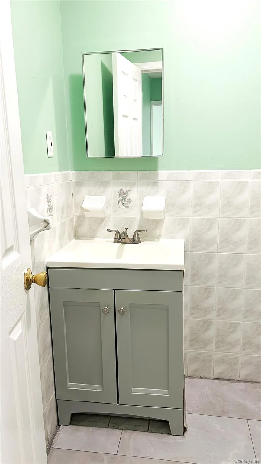 Bathroom featuring tile walls, wainscoting, vanity, and light tile patterned flooring Bathroom featuring tile walls, wainscoting, vanity, and light tile patterned flooring