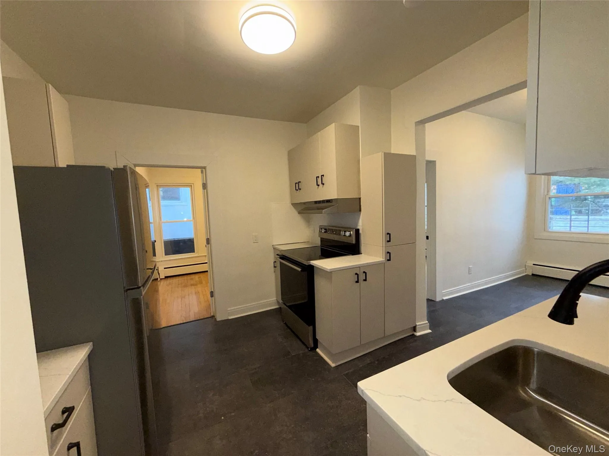 Kitchen featuring appliances with stainless steel finishes, light countertops, white cabinets, a baseboard heating unit, and plenty of natural light Kitchen featuring appliances with stainless steel finishes, light countertops, white cabinets, a baseboard heating unit, and plenty of natural light