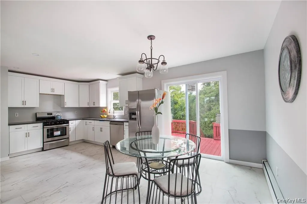 Kitchen featuring light marble finish flooring, appliances with stainless steel finishes, a baseboard radiator, white cabinets, and pendant lighting Kitchen featuring light marble finish flooring, appliances with stainless steel finishes, a baseboard radiator, white cabinets, and pendant lighting