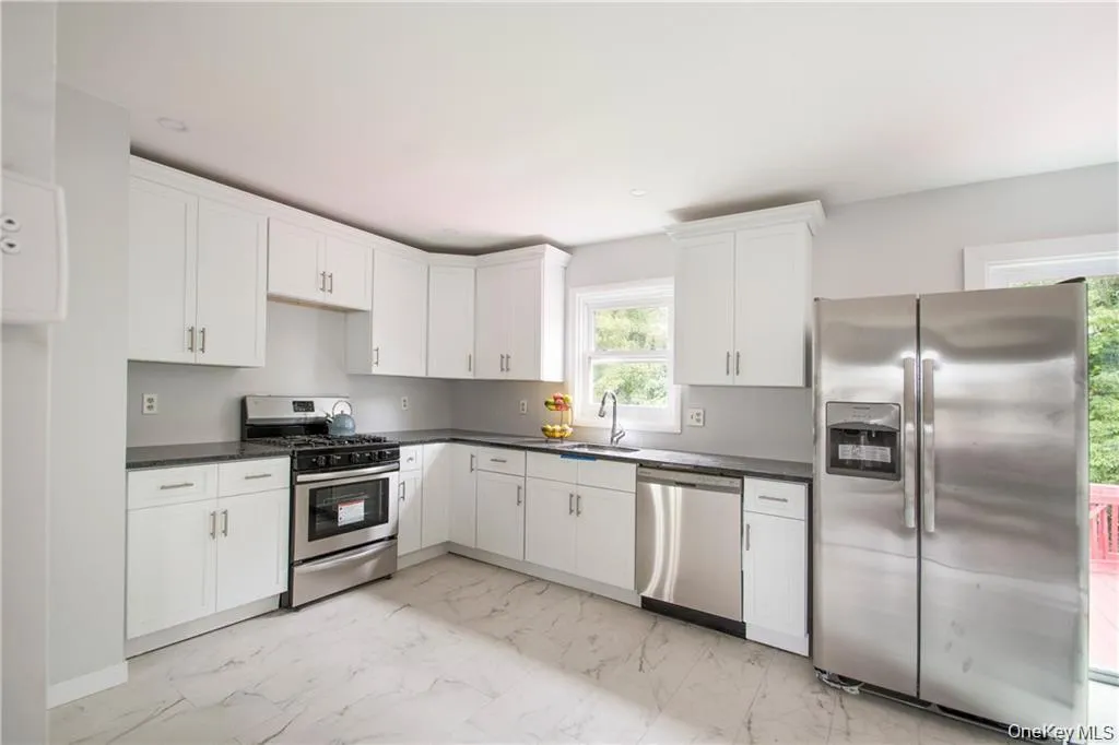 Kitchen with appliances with stainless steel finishes, light marble finish floors, white cabinetry, and dark countertops Kitchen with appliances with stainless steel finishes, light marble finish floors, white cabinetry, and dark countertops