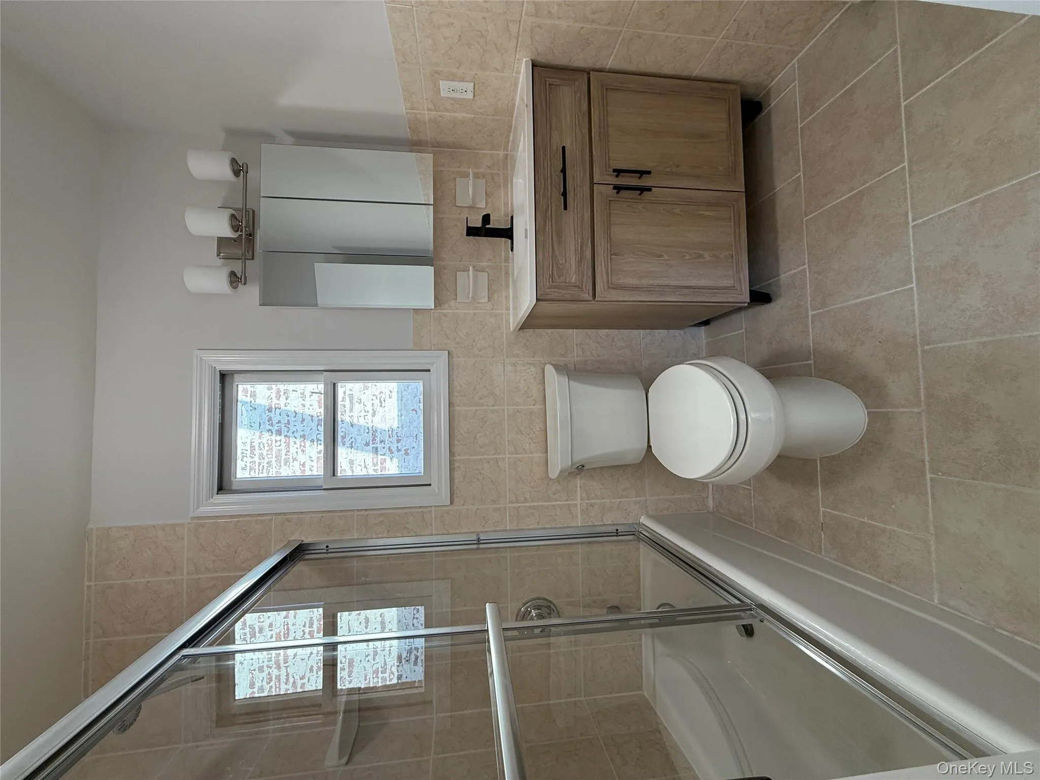 Bathroom with tile walls, vanity, enclosed tub / shower combo, light tile patterned floors, and a wainscoted wall Bathroom with tile walls, vanity, enclosed tub / shower combo, light tile patterned floors, and a wainscoted wall