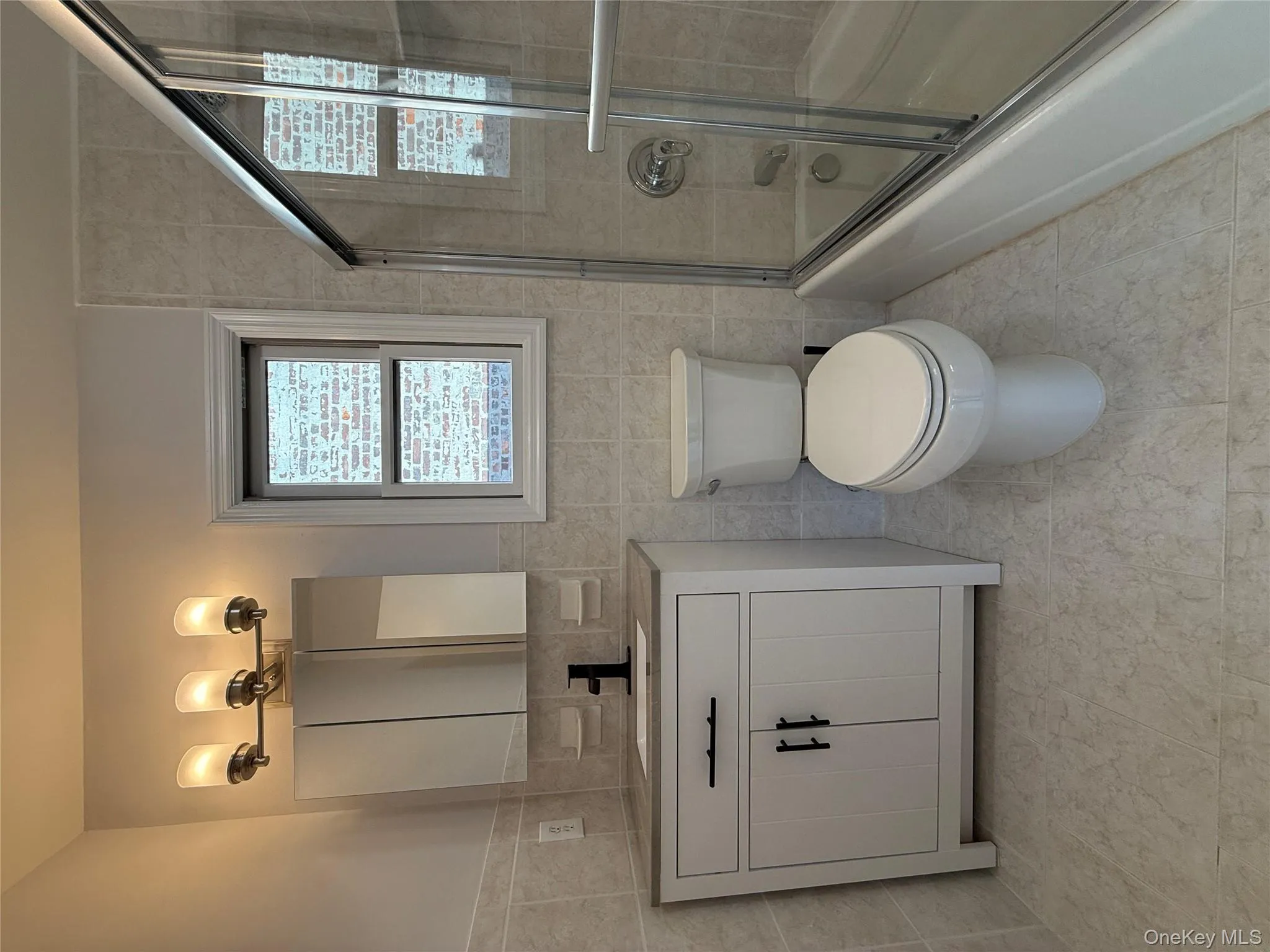 Full bath featuring tile walls, bath / shower combo with glass door, vanity, and light tile patterned flooring Full bath featuring tile walls, bath / shower combo with glass door, vanity, and light tile patterned flooring