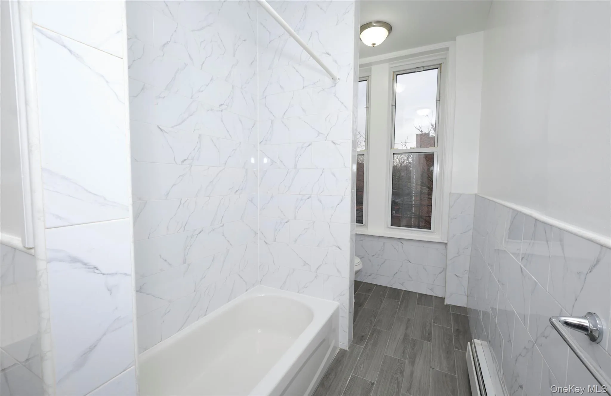 Bathroom with tile walls, a baseboard radiator, a wainscoted wall, and a combined bath / shower with marble appearance Bathroom with tile walls, a baseboard radiator, a wainscoted wall, and a combined bath / shower with marble appearance