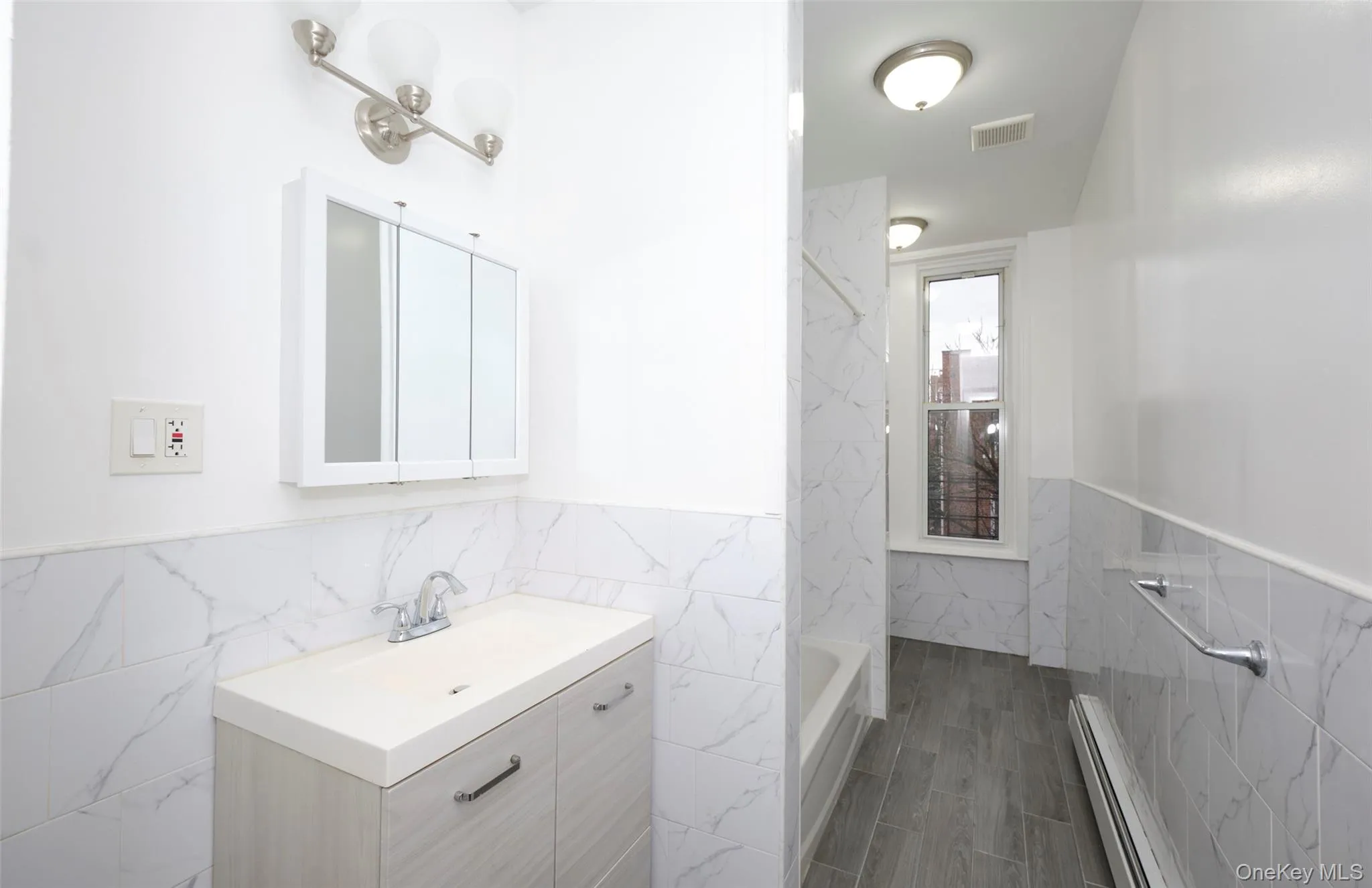 Full bathroom with tile walls, wainscoting, vanity, and baseboard heating Full bathroom with tile walls, wainscoting, vanity, and baseboard heating