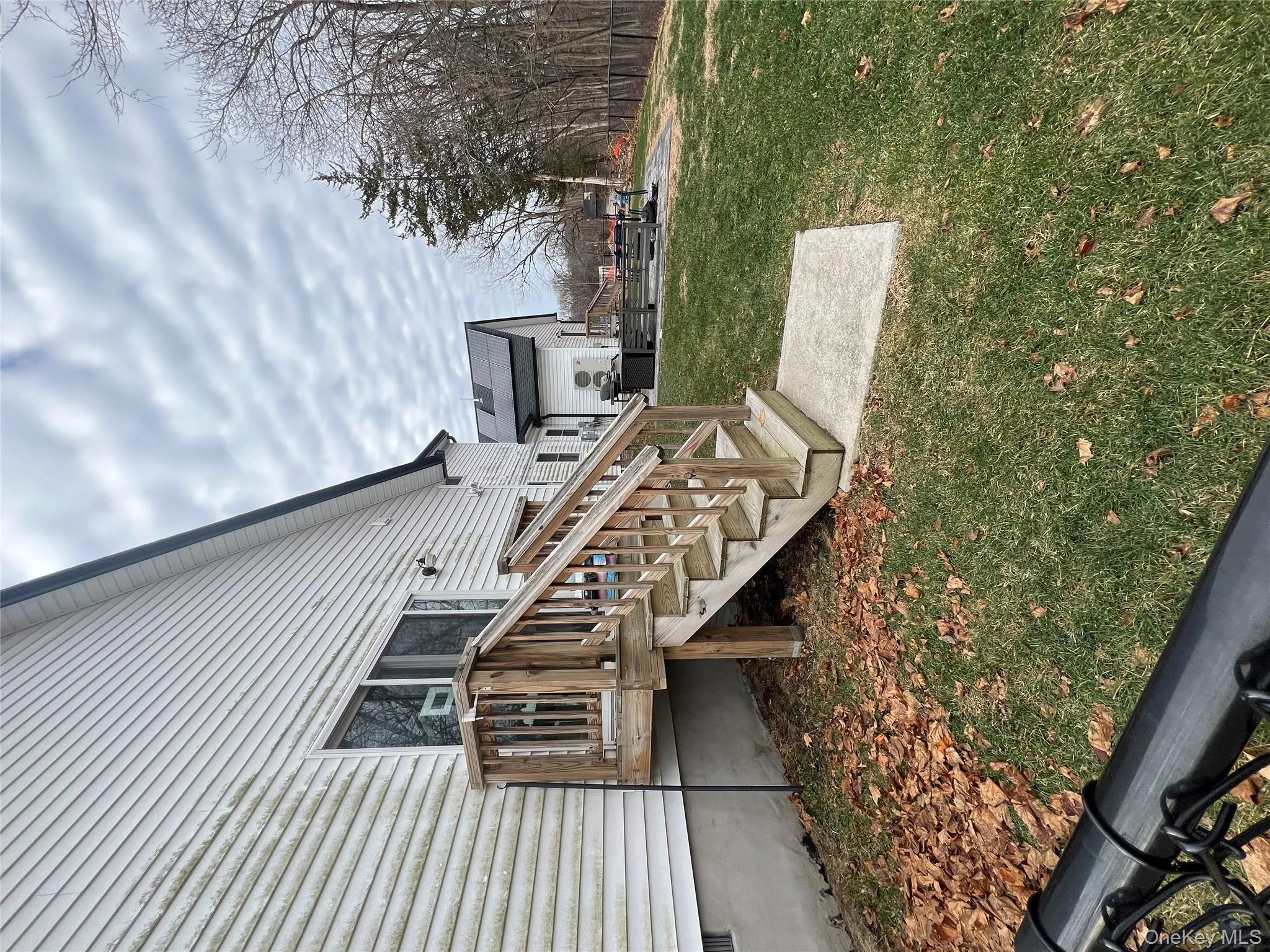 View of property exterior featuring a lawn, a deck, crawl space, stairs, and roof mounted solar panels View of property exterior featuring a lawn, a deck, crawl space, stairs, and roof mounted solar panels