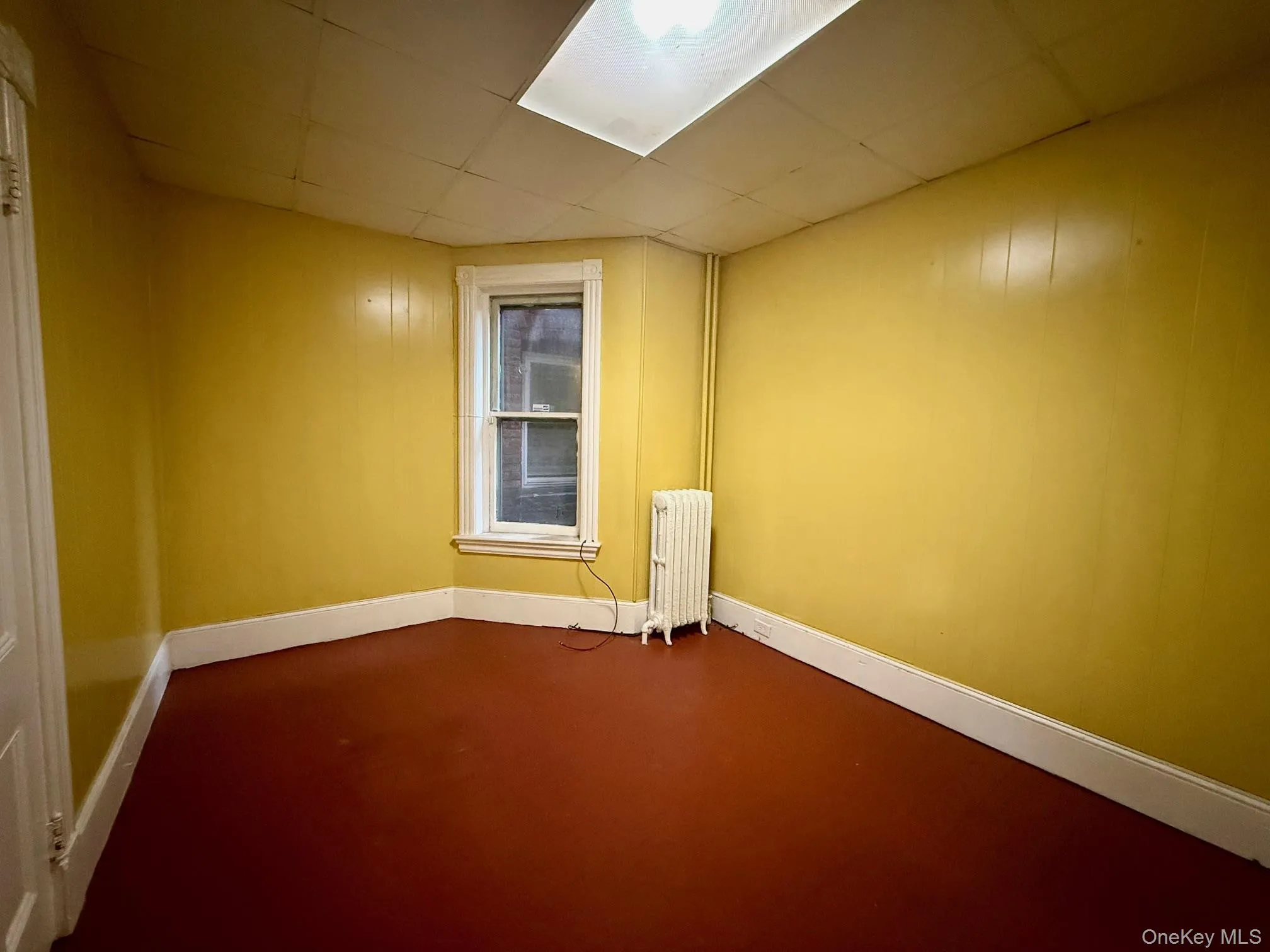 Empty room with finished concrete flooring, radiator heating unit, and wood walls Empty room with finished concrete flooring, radiator heating unit, and wood walls