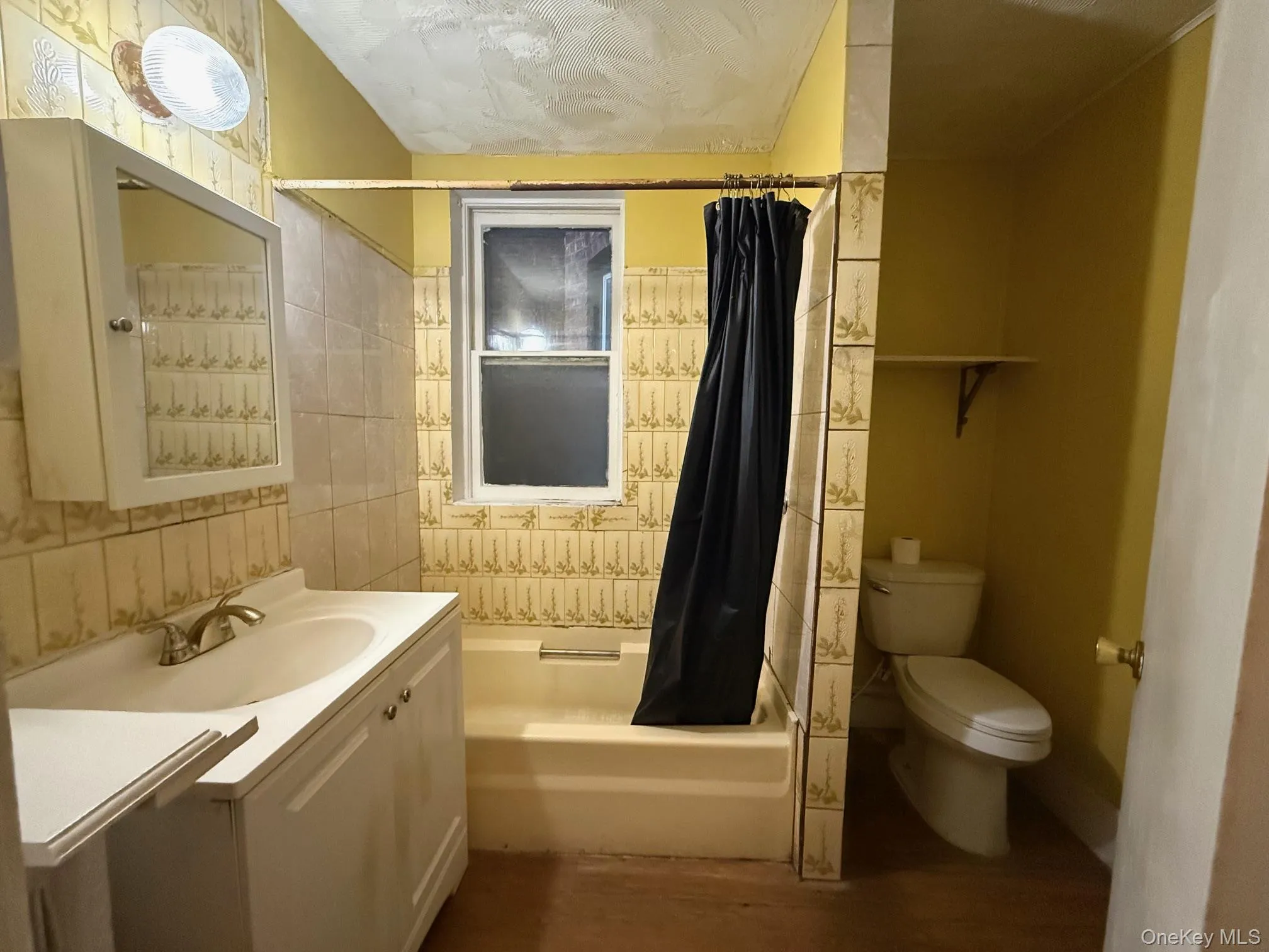 Bathroom with vanity, shower / bathtub combination with curtain, dark wood finished floors, and tile walls Bathroom with vanity, shower / bathtub combination with curtain, dark wood finished floors, and tile walls