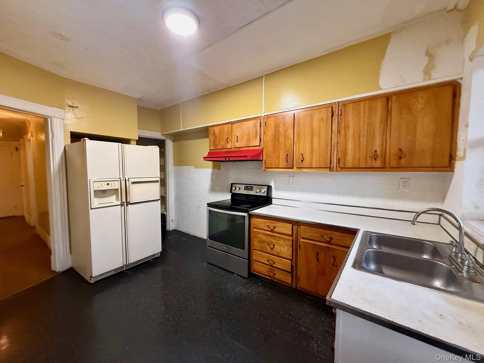 Kitchen with electric stove, white refrigerator with ice dispenser, brown cabinetry, light countertops, and under cabinet range hood Kitchen with electric stove, white refrigerator with ice dispenser, brown cabinetry, light countertops, and under cabinet range hood