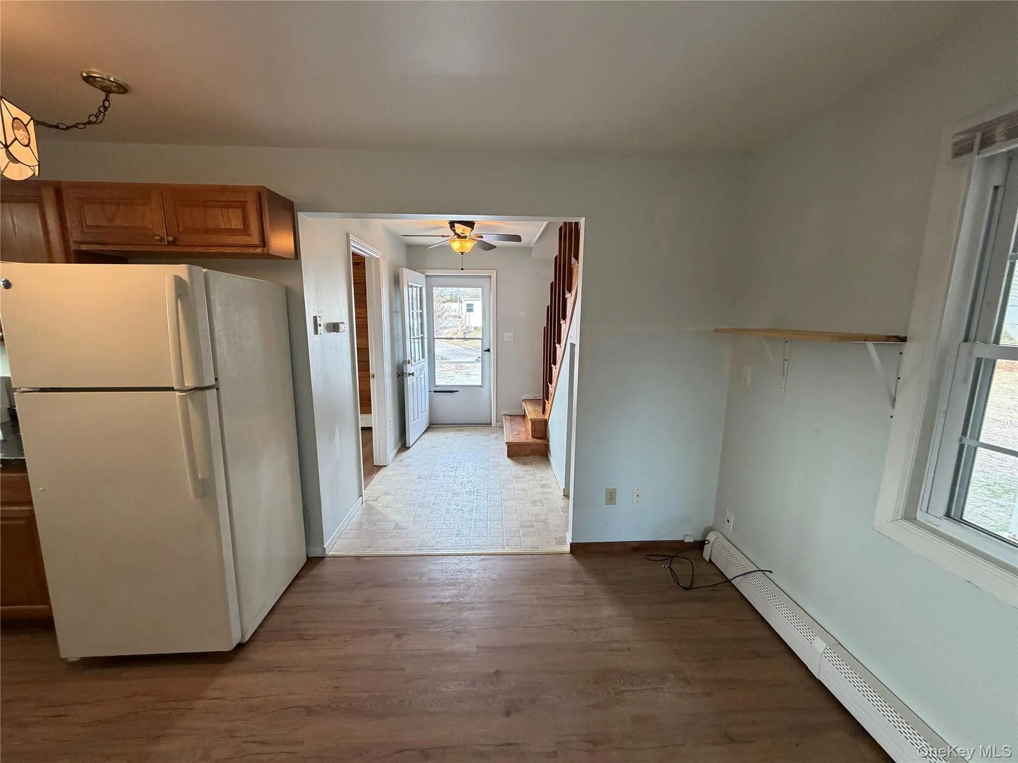 Kitchen with freestanding refrigerator, a baseboard heating unit, brown cabinetry, dark wood-style flooring, and ceiling fan Kitchen with freestanding refrigerator, a baseboard heating unit, brown cabinetry, dark wood-style flooring, and ceiling fan