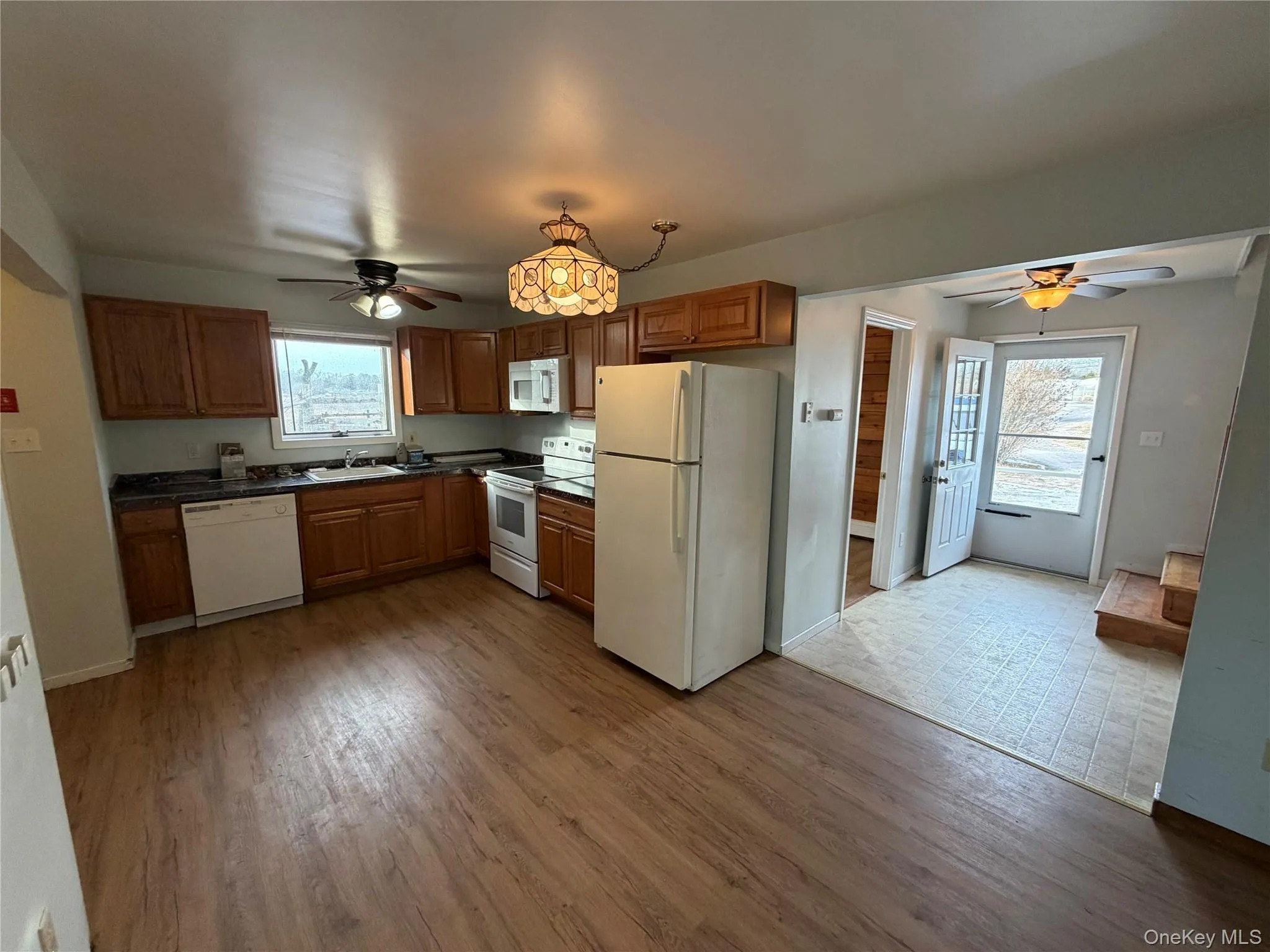 Kitchen featuring ceiling fan, white appliances, dark countertops, and brown cabinets Kitchen featuring ceiling fan, white appliances, dark countertops, and brown cabinets