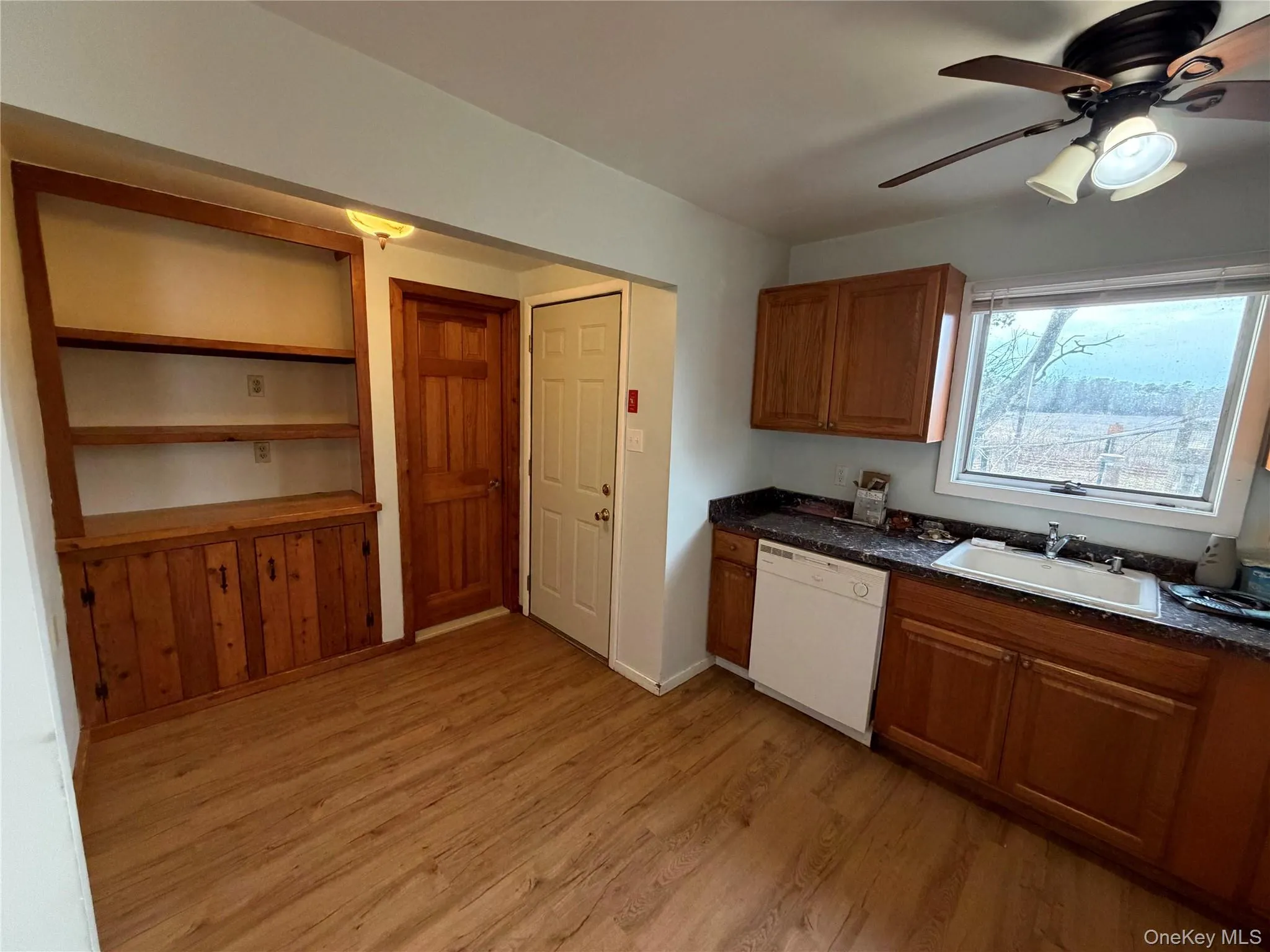 Kitchen featuring brown cabinetry, dishwasher, a ceiling fan, light wood-style flooring, and built in shelves Kitchen featuring brown cabinetry, dishwasher, a ceiling fan, light wood-style flooring, and built in shelves