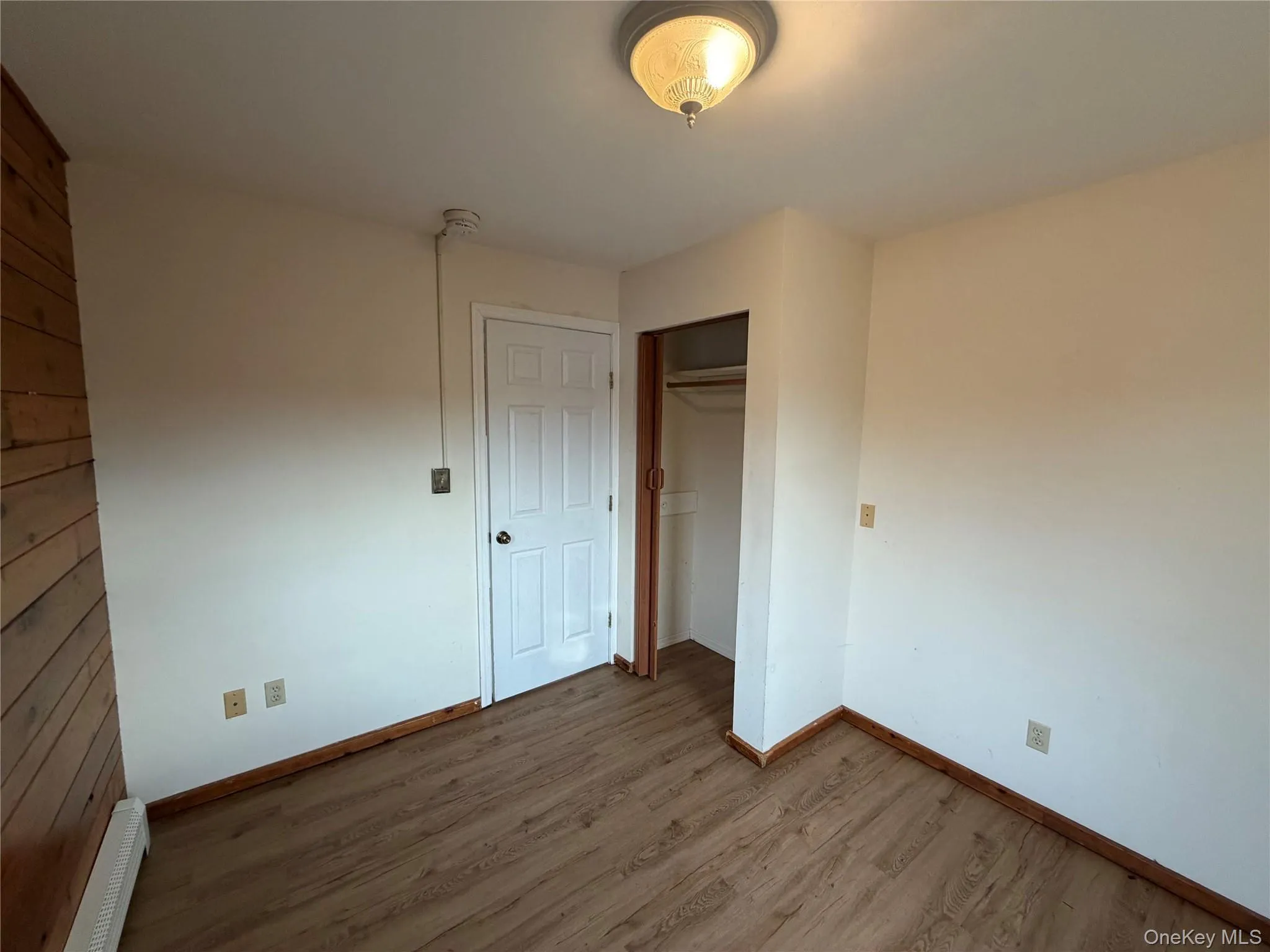 Unfurnished bedroom featuring a closet, wood finished floors, and a baseboard radiator Unfurnished bedroom featuring a closet, wood finished floors, and a baseboard radiator