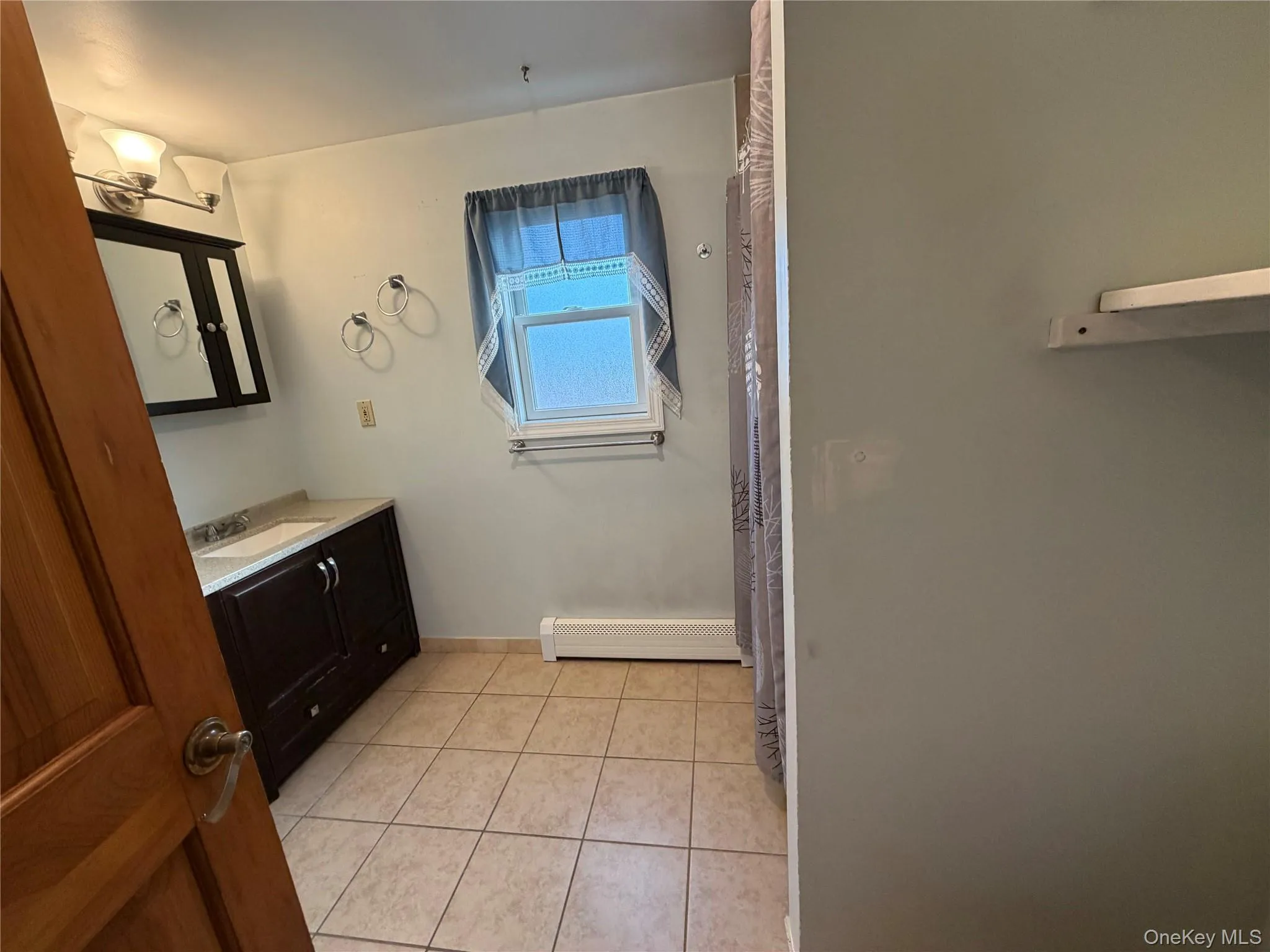 Full bath with vanity, light tile patterned flooring, baseboard heating, and curtained shower Full bath with vanity, light tile patterned flooring, baseboard heating, and curtained shower