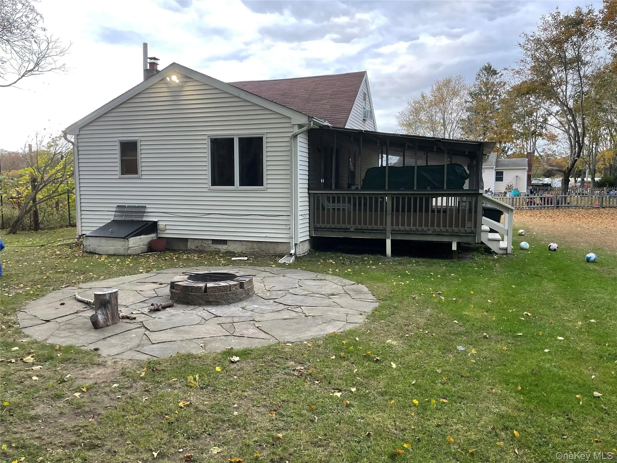 Rear view of house with a deck, a fire pit, a sunroom, a lawn, and a patio area Rear view of house with a deck, a fire pit, a sunroom, a lawn, and a patio area