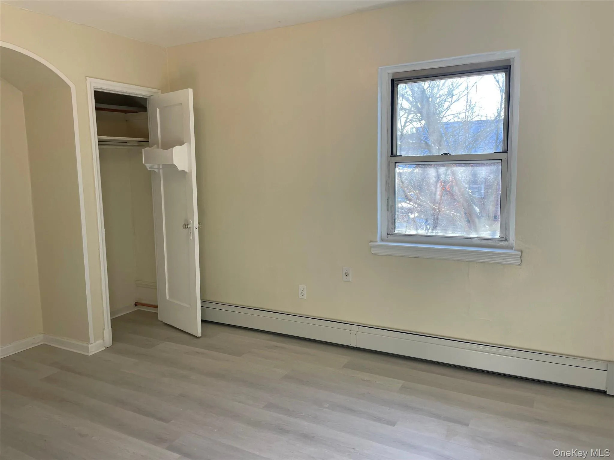 Unfurnished bedroom featuring baseboard heating, light wood-style floors, and a closet Unfurnished bedroom featuring baseboard heating, light wood-style floors, and a closet
