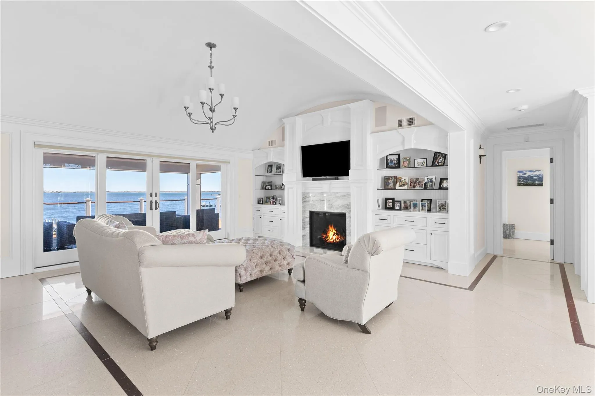 Living room with built in shelves, ornamental molding, inlaid floor details, a high end fireplace, and french doors Living room with built in shelves, ornamental molding, inlaid floor details, a high end fireplace, and french doors