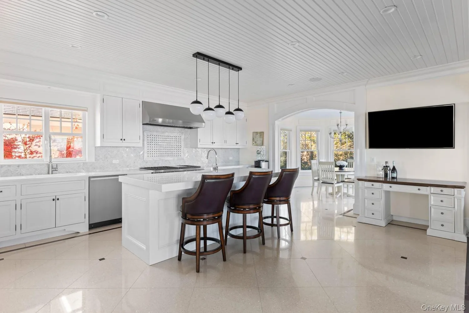 Kitchen featuring white cabinets, decorative light fixtures, a kitchen island with sink, arched walkways, and a breakfast bar Kitchen featuring white cabinets, decorative light fixtures, a kitchen island with sink, arched walkways, and a breakfast bar