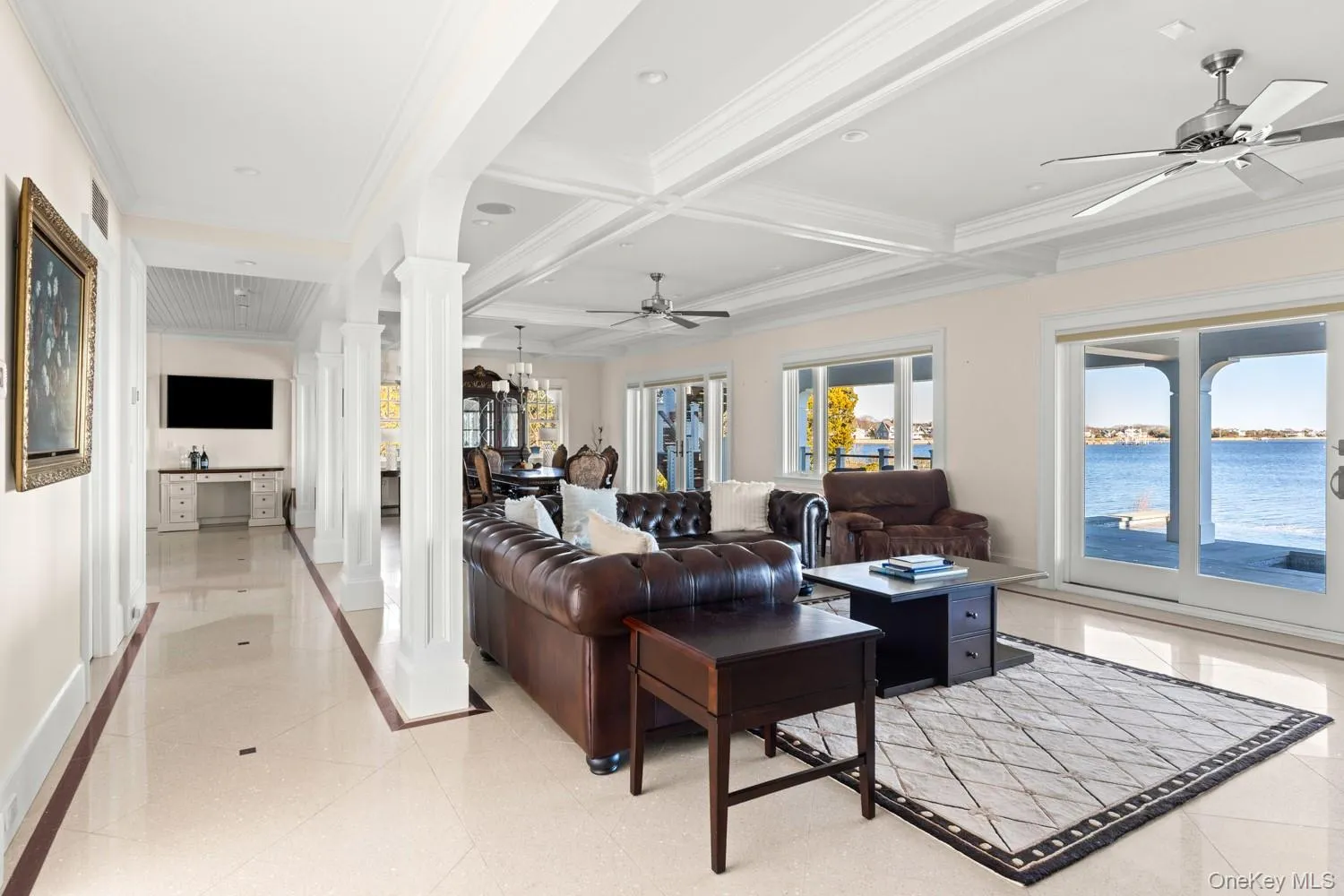 Living room with a ceiling fan, decorative columns, crown molding, a water view, and coffered ceiling Living room with a ceiling fan, decorative columns, crown molding, a water view, and coffered ceiling