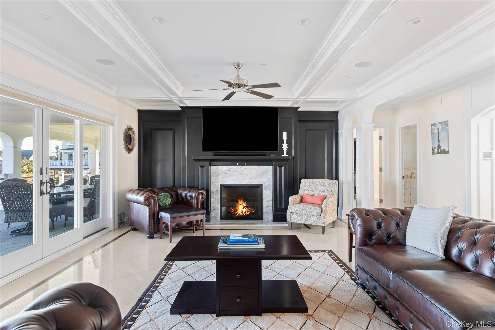 Living room with inlaid floor details, a lit fireplace, ceiling fan, crown molding, and beamed ceiling Living room with inlaid floor details, a lit fireplace, ceiling fan, crown molding, and beamed ceiling