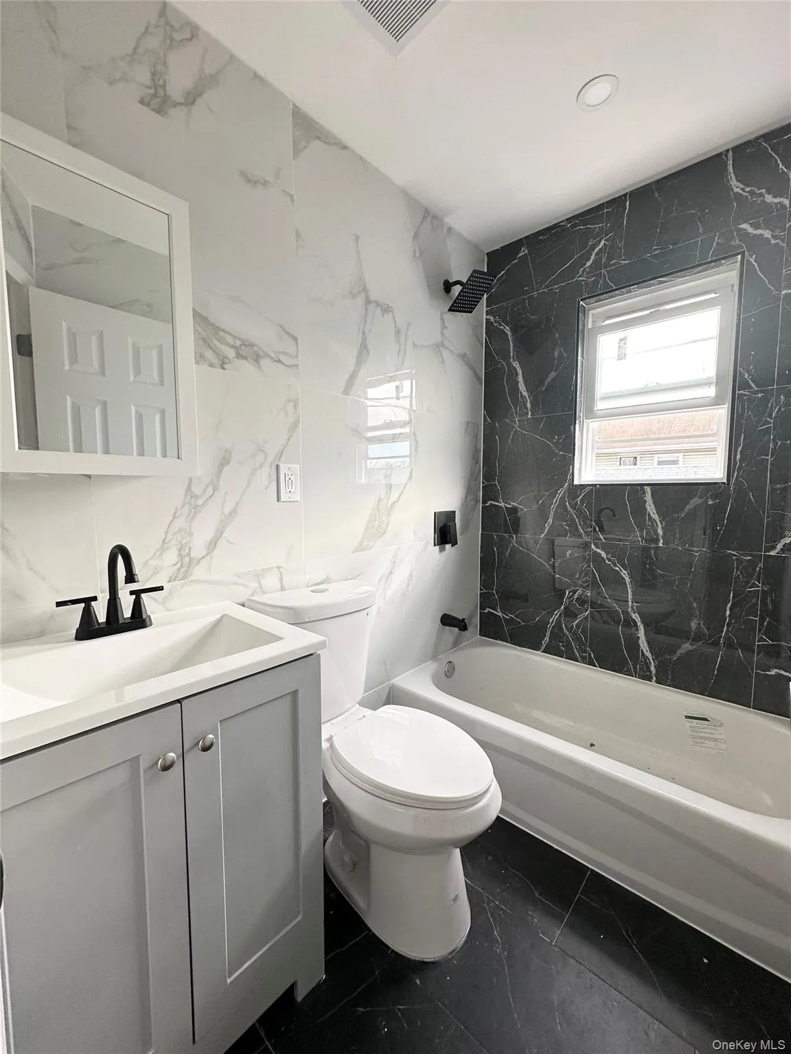 Full bath with tile walls, dark marble finish floors, vanity, tub / shower combination, and stone wall Full bath with tile walls, dark marble finish floors, vanity, tub / shower combination, and stone wall