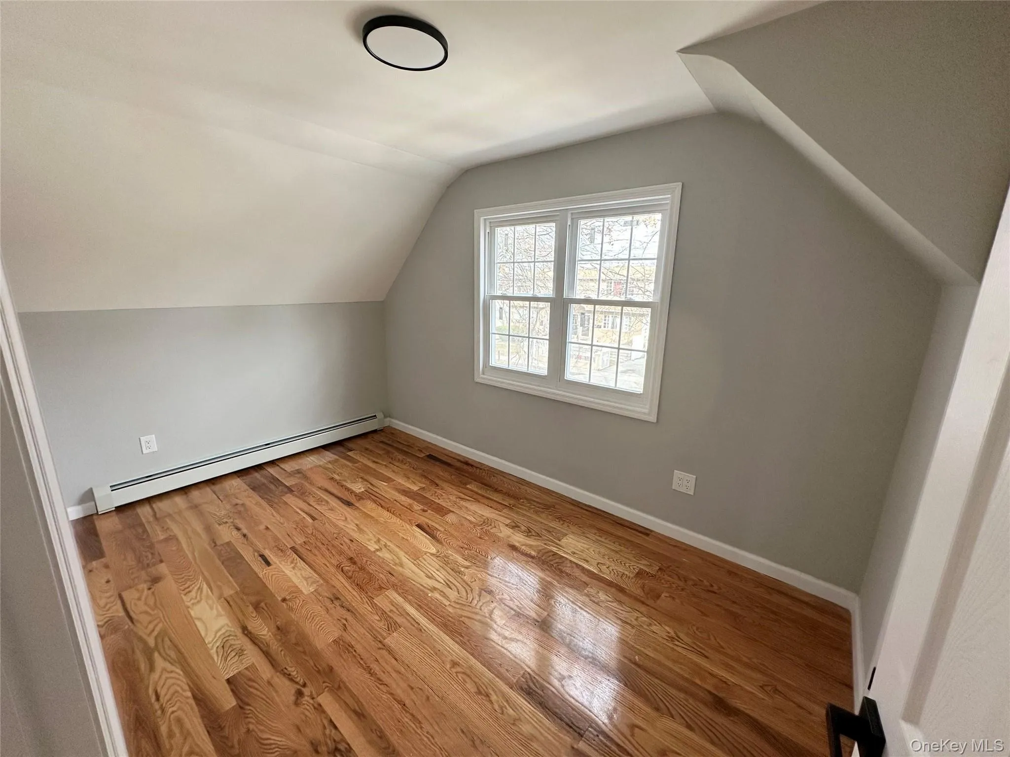 Additional living space with a baseboard radiator, light wood finished floors, and lofted ceiling Additional living space with a baseboard radiator, light wood finished floors, and lofted ceiling