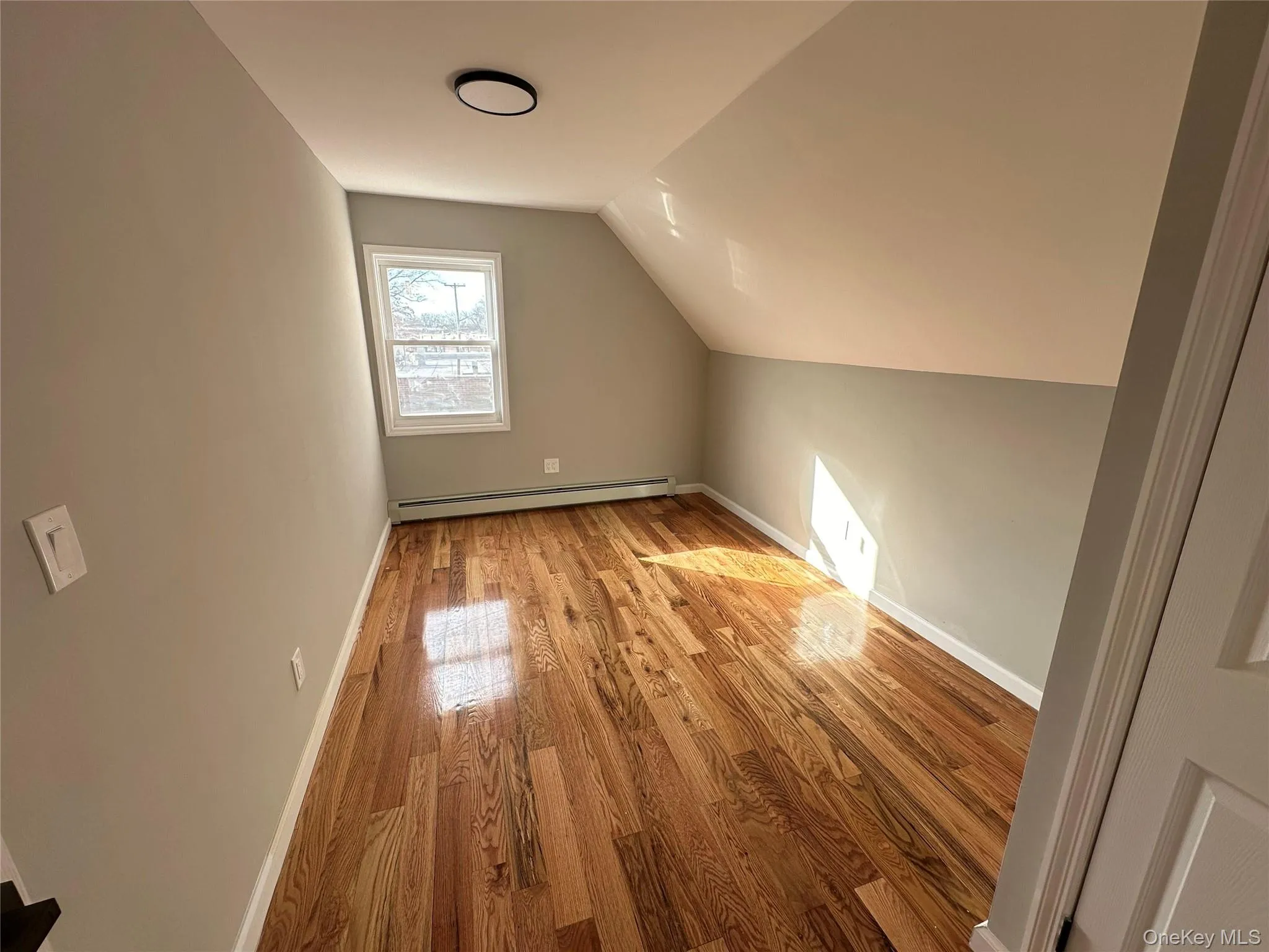 Bonus room with light wood-style floors, vaulted ceiling, and a baseboard radiator Bonus room with light wood-style floors, vaulted ceiling, and a baseboard radiator
