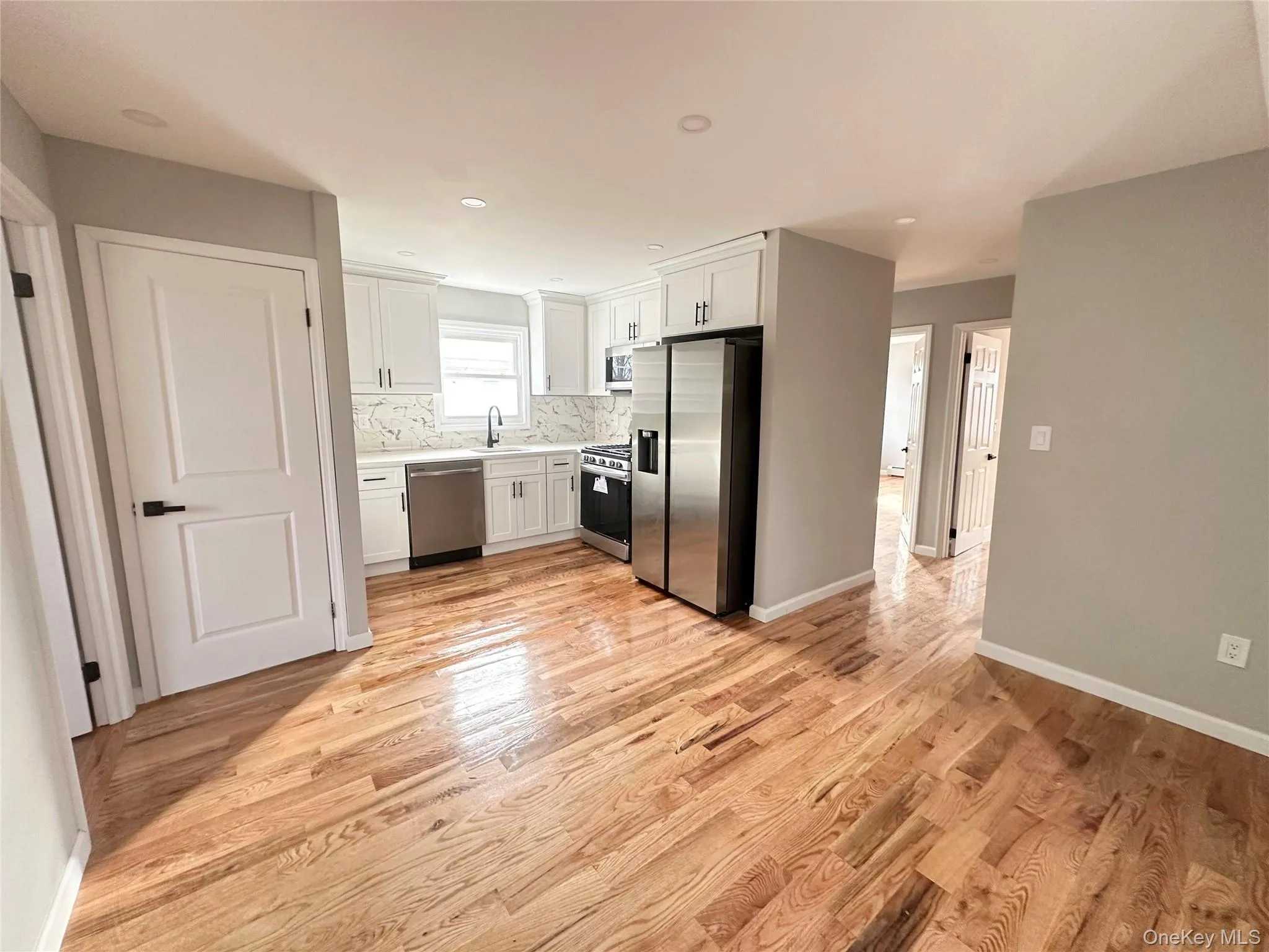 Kitchen with stainless steel appliances, white cabinetry, light countertops, light wood-style floors, and backsplash Kitchen with stainless steel appliances, white cabinetry, light countertops, light wood-style floors, and backsplash