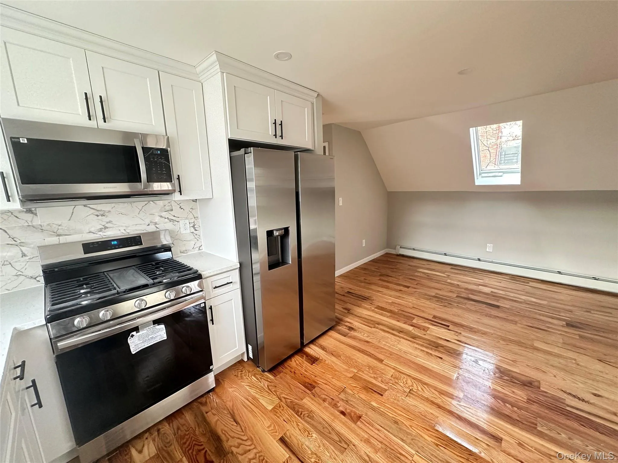 Kitchen with white cabinets, appliances with stainless steel finishes, tasteful backsplash, vaulted ceiling, and a skylight Kitchen with white cabinets, appliances with stainless steel finishes, tasteful backsplash, vaulted ceiling, and a skylight