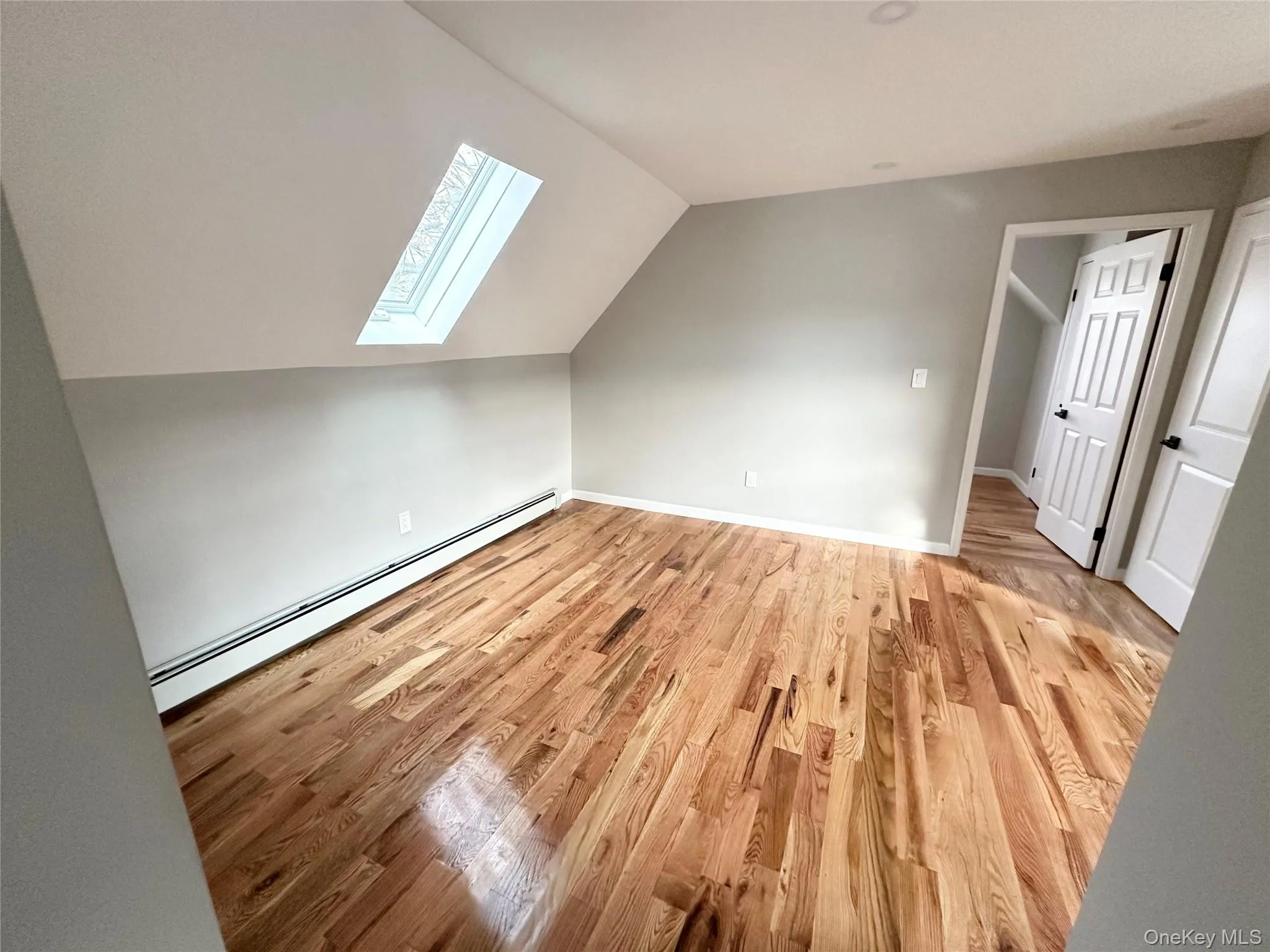Additional living space featuring a baseboard heating unit, light wood finished floors, lofted ceiling, and a skylight Additional living space featuring a baseboard heating unit, light wood finished floors, lofted ceiling, and a skylight