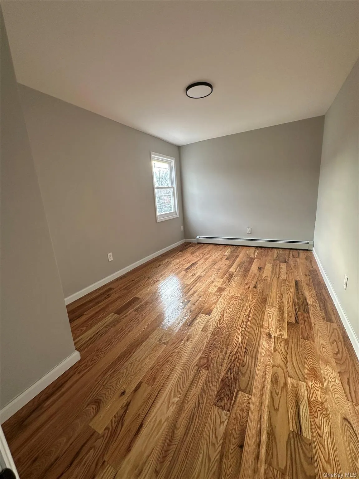 Unfurnished room featuring light wood-style flooring and a baseboard heating unit Unfurnished room featuring light wood-style flooring and a baseboard heating unit