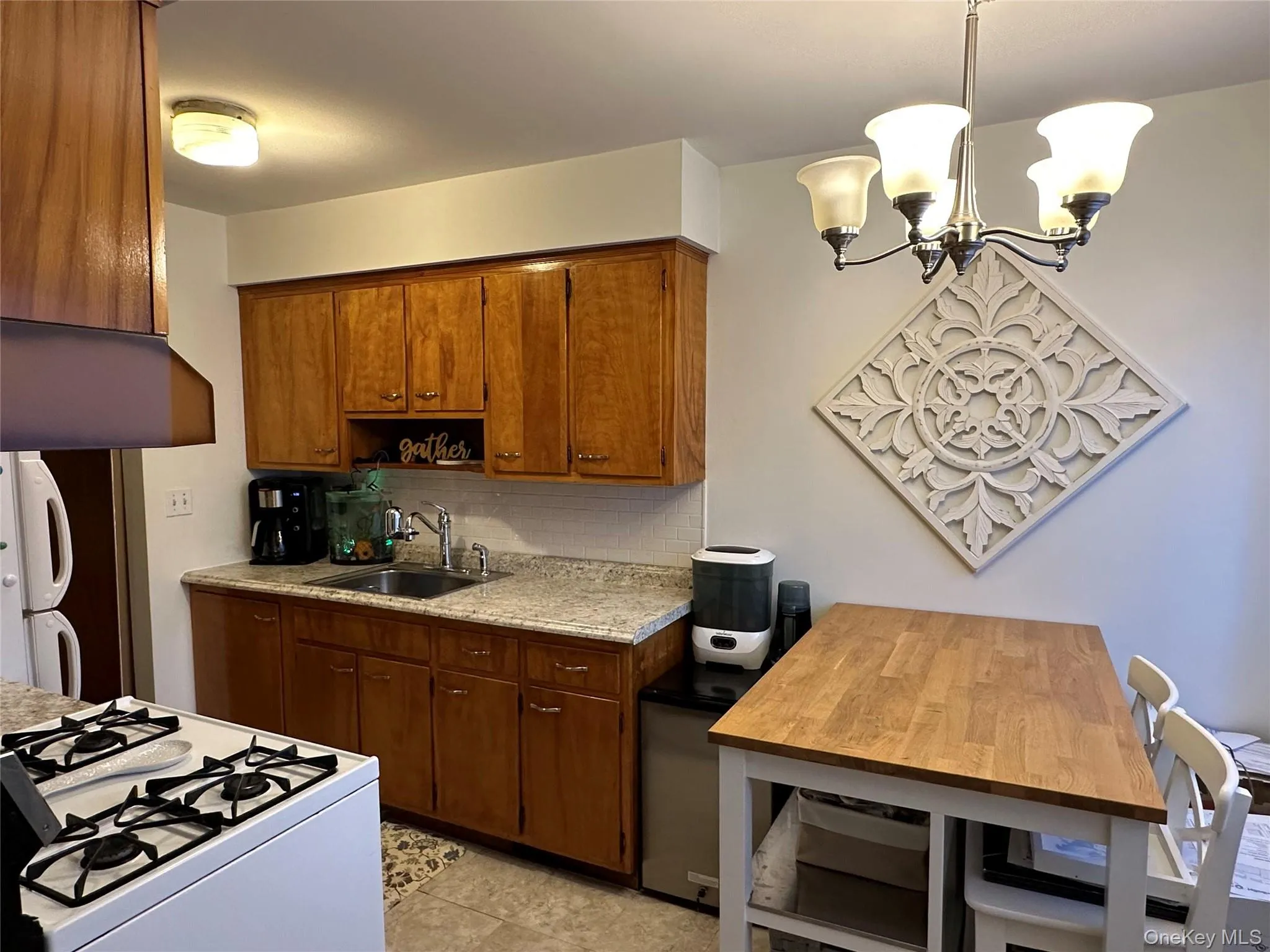 Kitchen with white appliances, brown cabinets, hanging light fixtures, and a chandelier Kitchen with white appliances, brown cabinets, hanging light fixtures, and a chandelier
