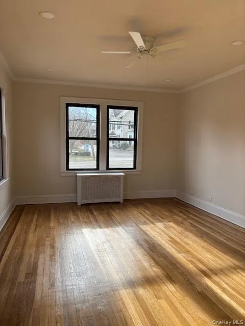 Unfurnished room featuring radiator heating unit, a ceiling fan, crown molding, and light wood-style floors Unfurnished room featuring radiator heating unit, a ceiling fan, crown molding, and light wood-style floors
