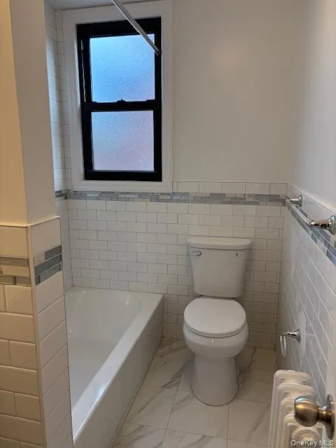 Bathroom with wainscoting, radiator, tile walls, and light marble finish flooring Bathroom with wainscoting, radiator, tile walls, and light marble finish flooring