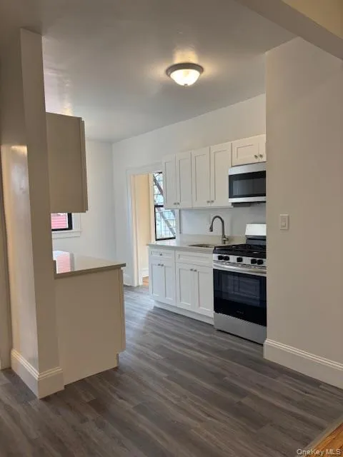 Kitchen with appliances with stainless steel finishes, light countertops, dark wood-style flooring, and white cabinets Kitchen with appliances with stainless steel finishes, light countertops, dark wood-style flooring, and white cabinets