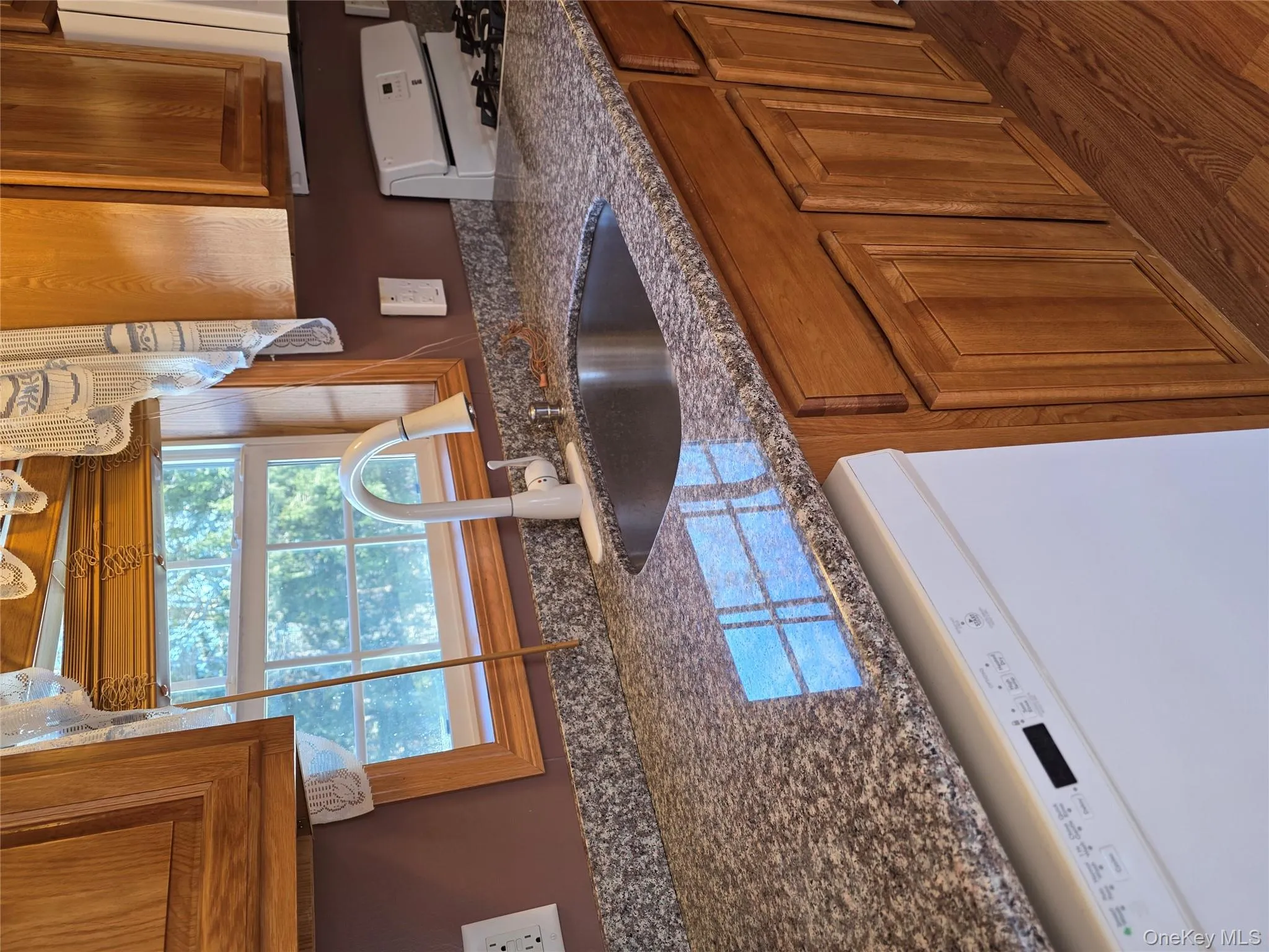Kitchen featuring dishwashing machine, brown cabinets, and dark stone counters Kitchen featuring dishwashing machine, brown cabinets, and dark stone counters