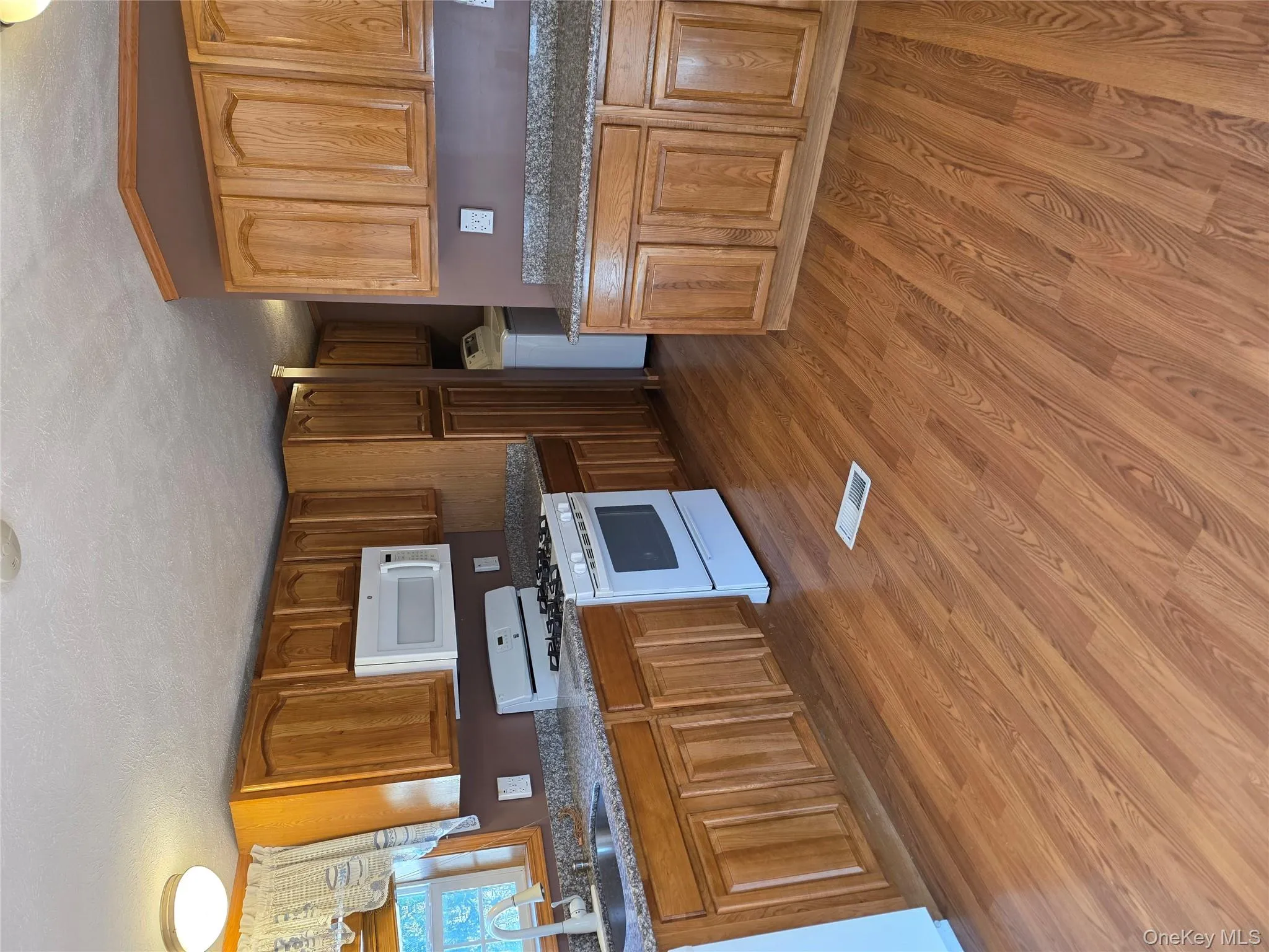 Kitchen with white range oven, dark stone countertops, brown cabinetry, light wood-type flooring, and washer / clothes dryer Kitchen with white range oven, dark stone countertops, brown cabinetry, light wood-type flooring, and washer / clothes dryer