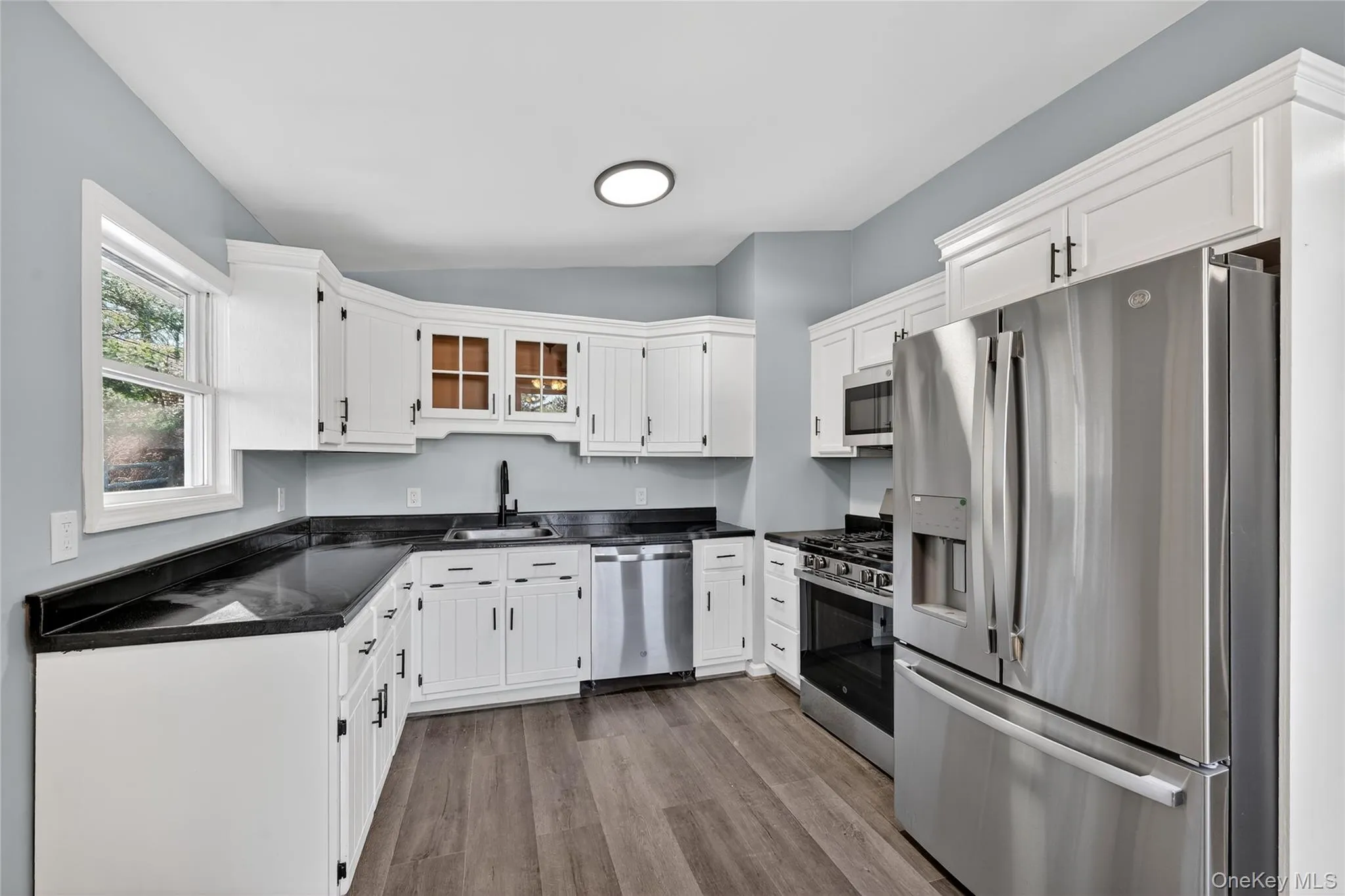 Kitchen with appliances with stainless steel finishes, white cabinetry, vaulted ceiling, dark wood-type flooring, and glass insert cabinets Kitchen with appliances with stainless steel finishes, white cabinetry, vaulted ceiling, dark wood-type flooring, and glass insert cabinets