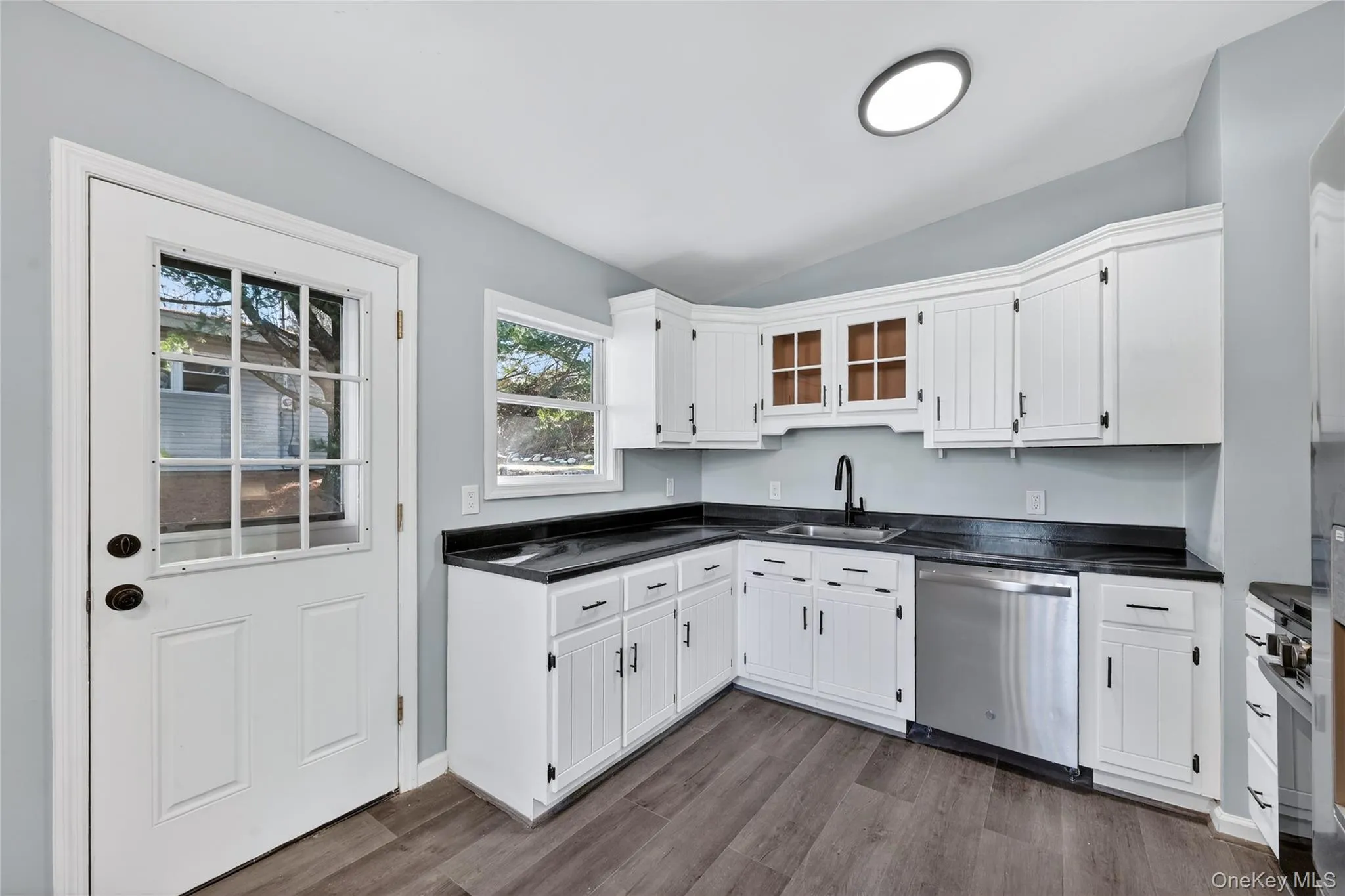 Kitchen featuring dark countertops, stainless steel appliances, white cabinetry, vaulted ceiling, and dark wood-type flooring Kitchen featuring dark countertops, stainless steel appliances, white cabinetry, vaulted ceiling, and dark wood-type flooring