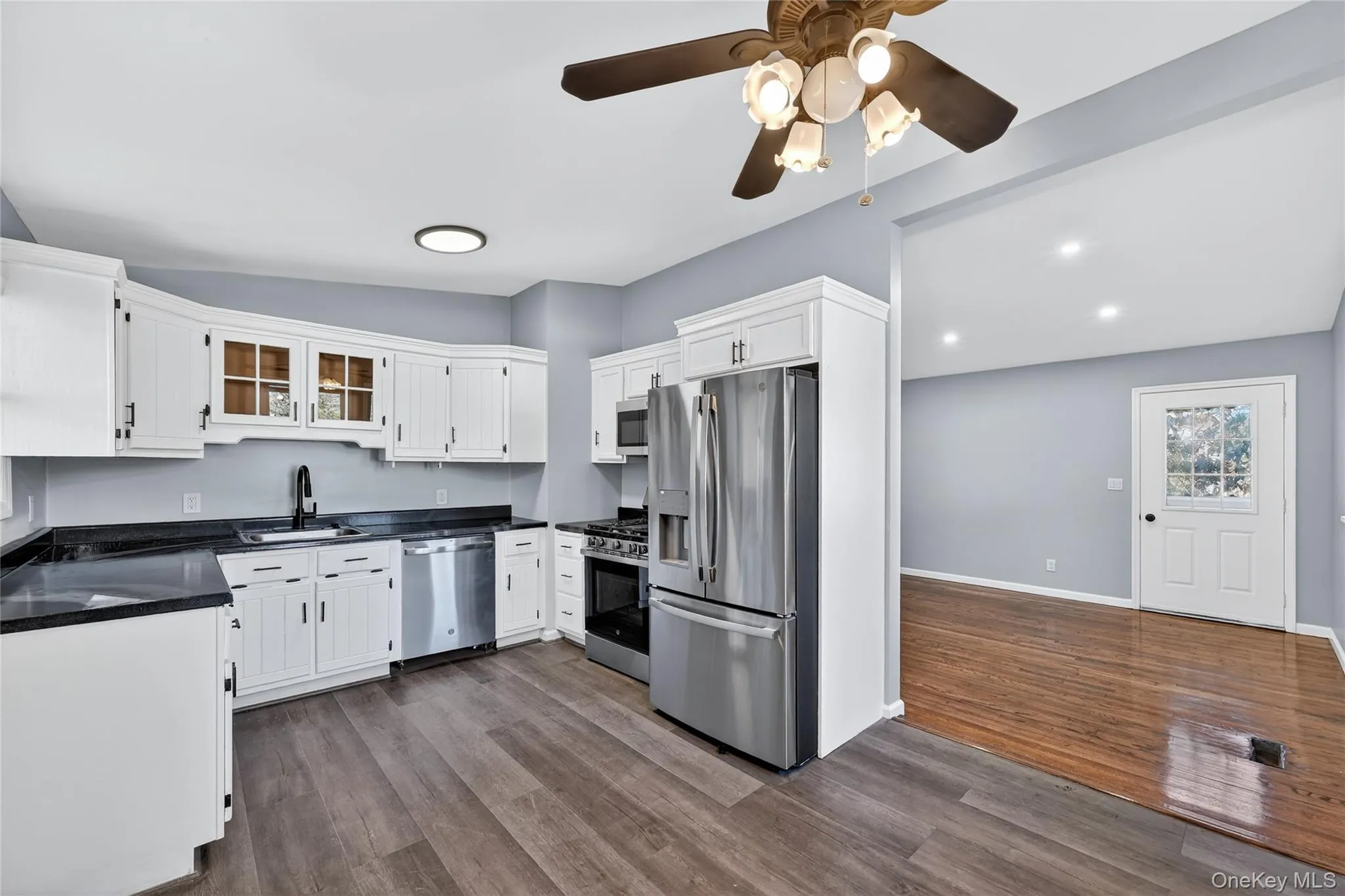 Kitchen featuring appliances with stainless steel finishes, white cabinets, dark wood-style flooring, glass insert cabinets, and vaulted ceiling Kitchen featuring appliances with stainless steel finishes, white cabinets, dark wood-style flooring, glass insert cabinets, and vaulted ceiling