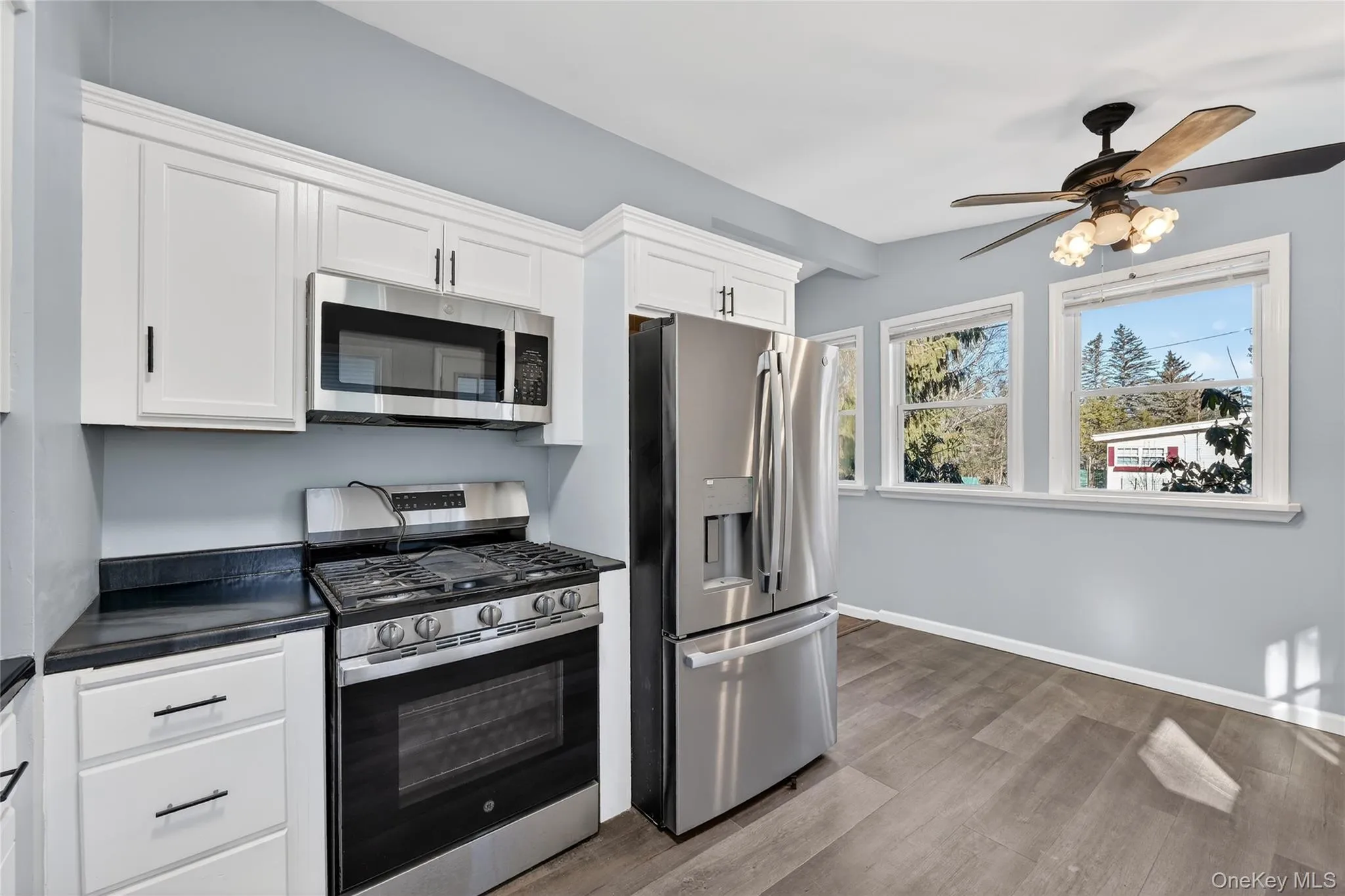 Kitchen featuring appliances with stainless steel finishes, dark countertops, white cabinets, light wood finished floors, and a ceiling fan Kitchen featuring appliances with stainless steel finishes, dark countertops, white cabinets, light wood finished floors, and a ceiling fan