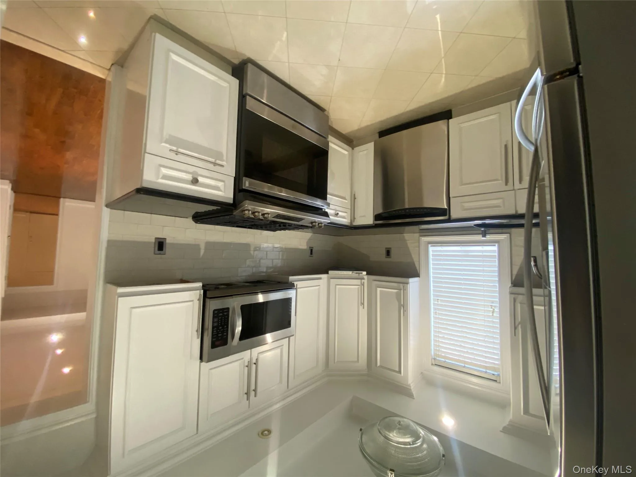 Kitchen featuring stainless steel appliances, white cabinets, tasteful backsplash, light tile patterned floors, and dark stone counters Kitchen featuring stainless steel appliances, white cabinets, tasteful backsplash, light tile patterned floors, and dark stone counters