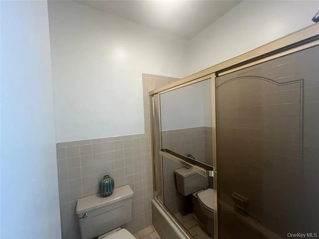 Full bathroom with tile walls and bath / shower combo with glass door Full bathroom with tile walls and bath / shower combo with glass door