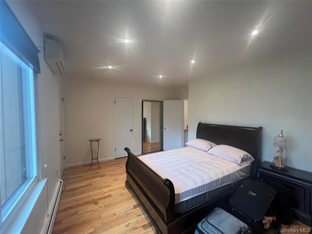 Bedroom with a baseboard radiator, light wood-style flooring, and a wall mounted air conditioner Bedroom with a baseboard radiator, light wood-style flooring, and a wall mounted air conditioner