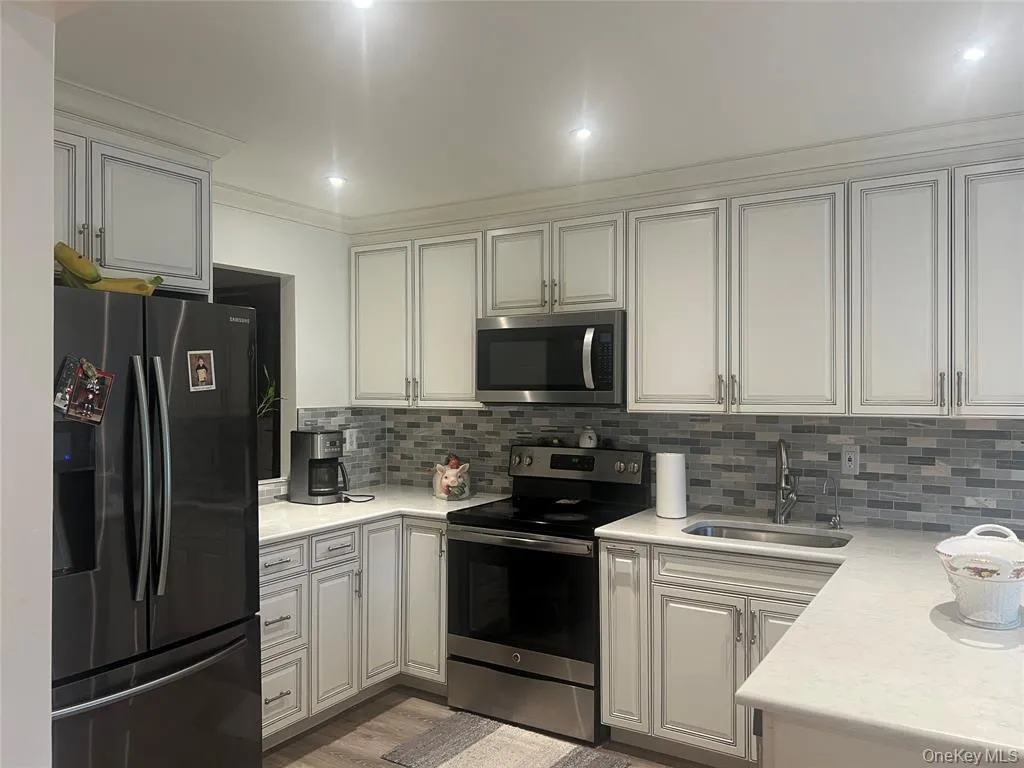 Kitchen featuring appliances with stainless steel finishes, light stone counters, white cabinets, light wood-style floors, and backsplash Kitchen featuring appliances with stainless steel finishes, light stone counters, white cabinets, light wood-style floors, and backsplash