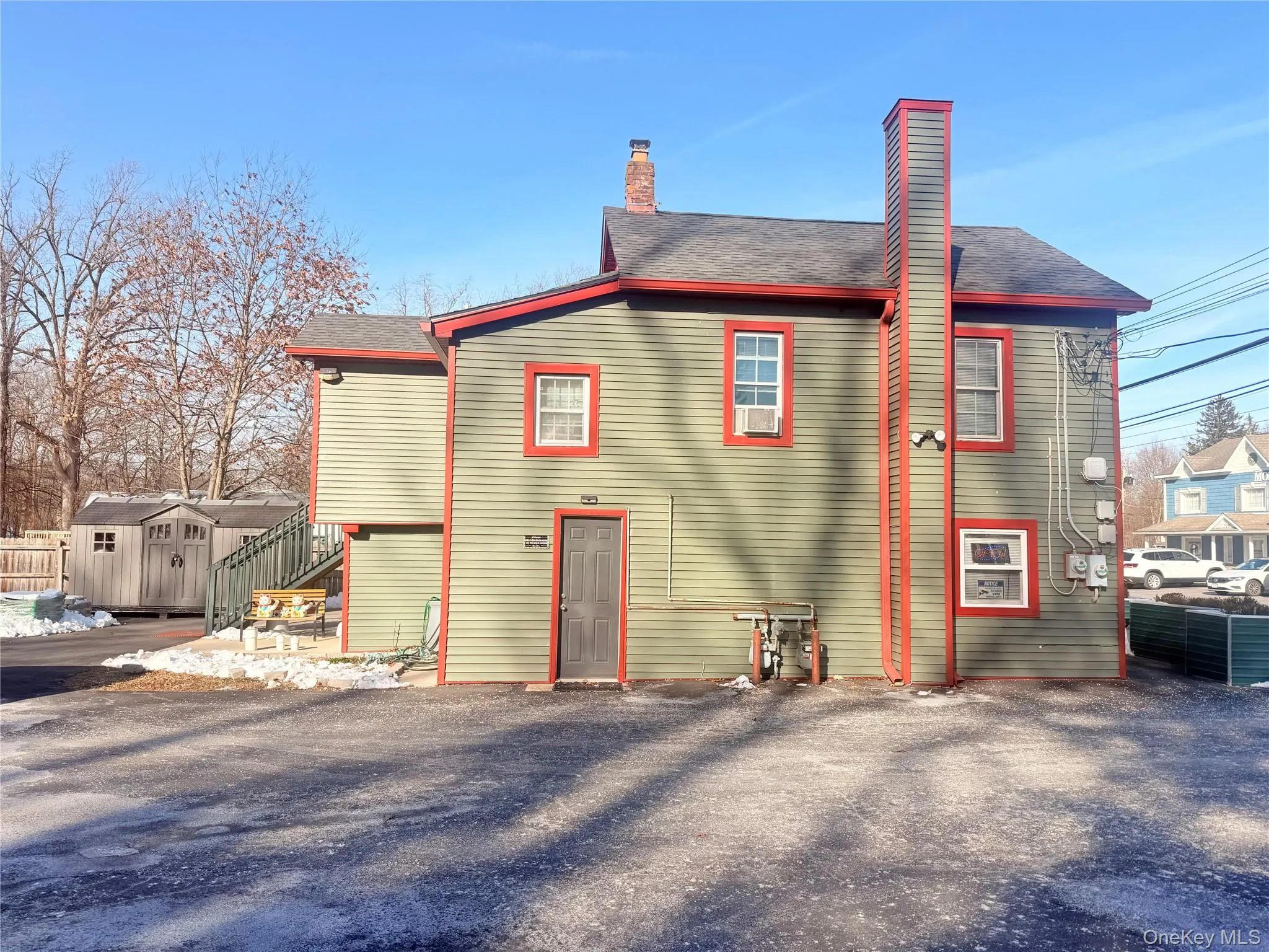 Rear view of property featuring a chimney, a shingled roof, a shed, and stairs Rear view of property featuring a chimney, a shingled roof, a shed, and stairs