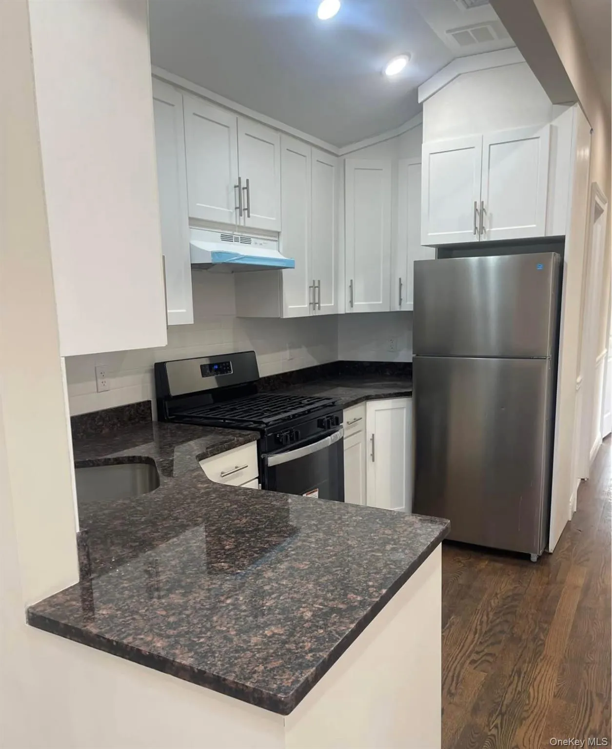 Kitchen featuring appliances with stainless steel finishes, dark stone countertops, white cabinets, dark wood finished floors, and under cabinet range hood Kitchen featuring appliances with stainless steel finishes, dark stone countertops, white cabinets, dark wood finished floors, and under cabinet range hood