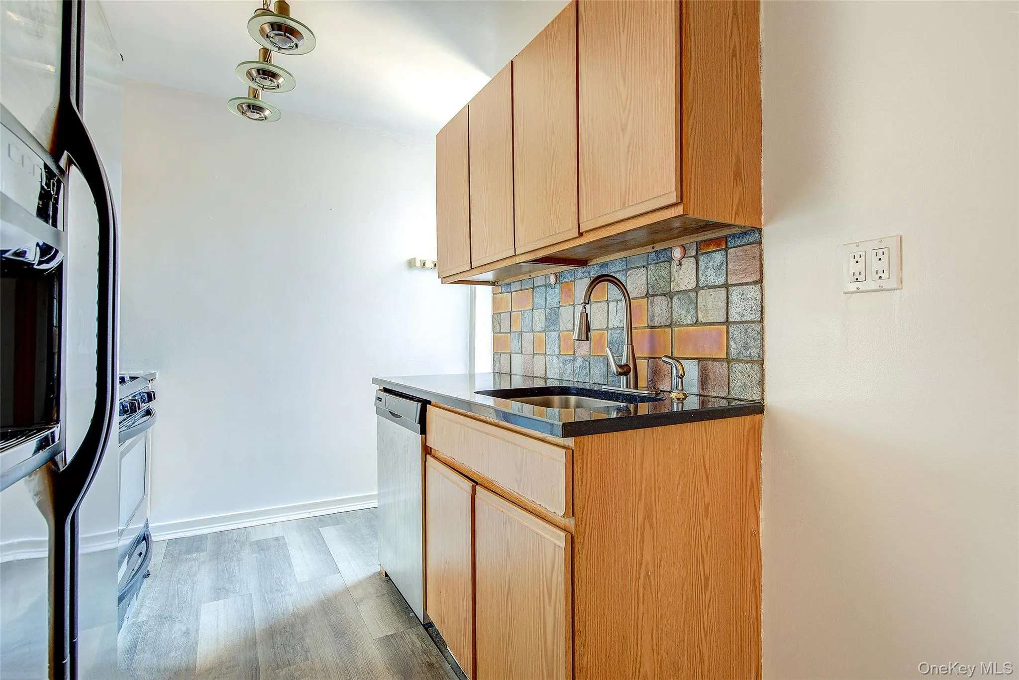 Kitchen with tasteful backsplash, dark stone counters, light wood-style floors, stainless steel appliances, and light brown cabinets Kitchen with tasteful backsplash, dark stone counters, light wood-style floors, stainless steel appliances, and light brown cabinets