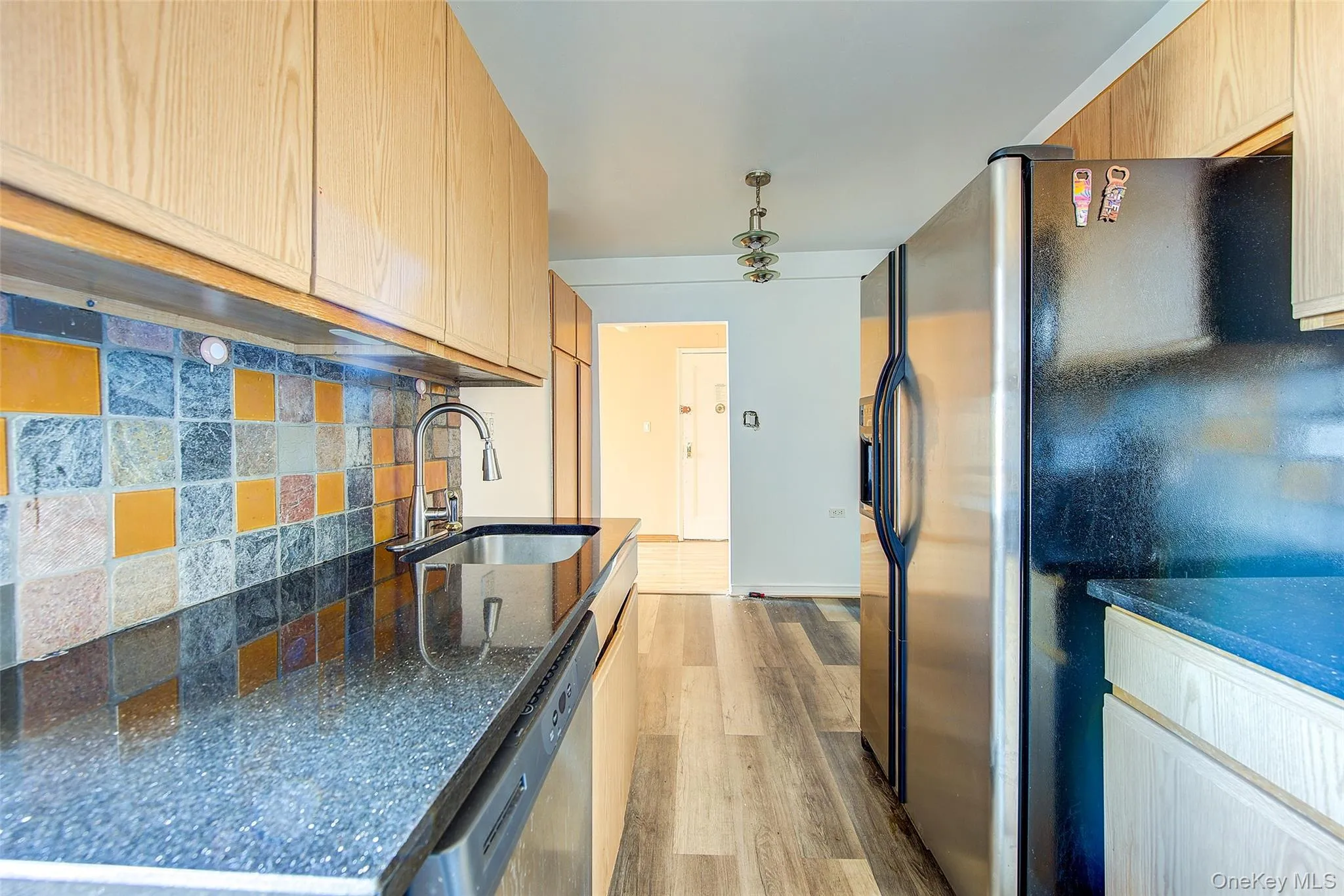 Kitchen with fridge with ice dispenser, tasteful backsplash, dishwasher, dark stone counters, and light wood-type flooring Kitchen with fridge with ice dispenser, tasteful backsplash, dishwasher, dark stone counters, and light wood-type flooring